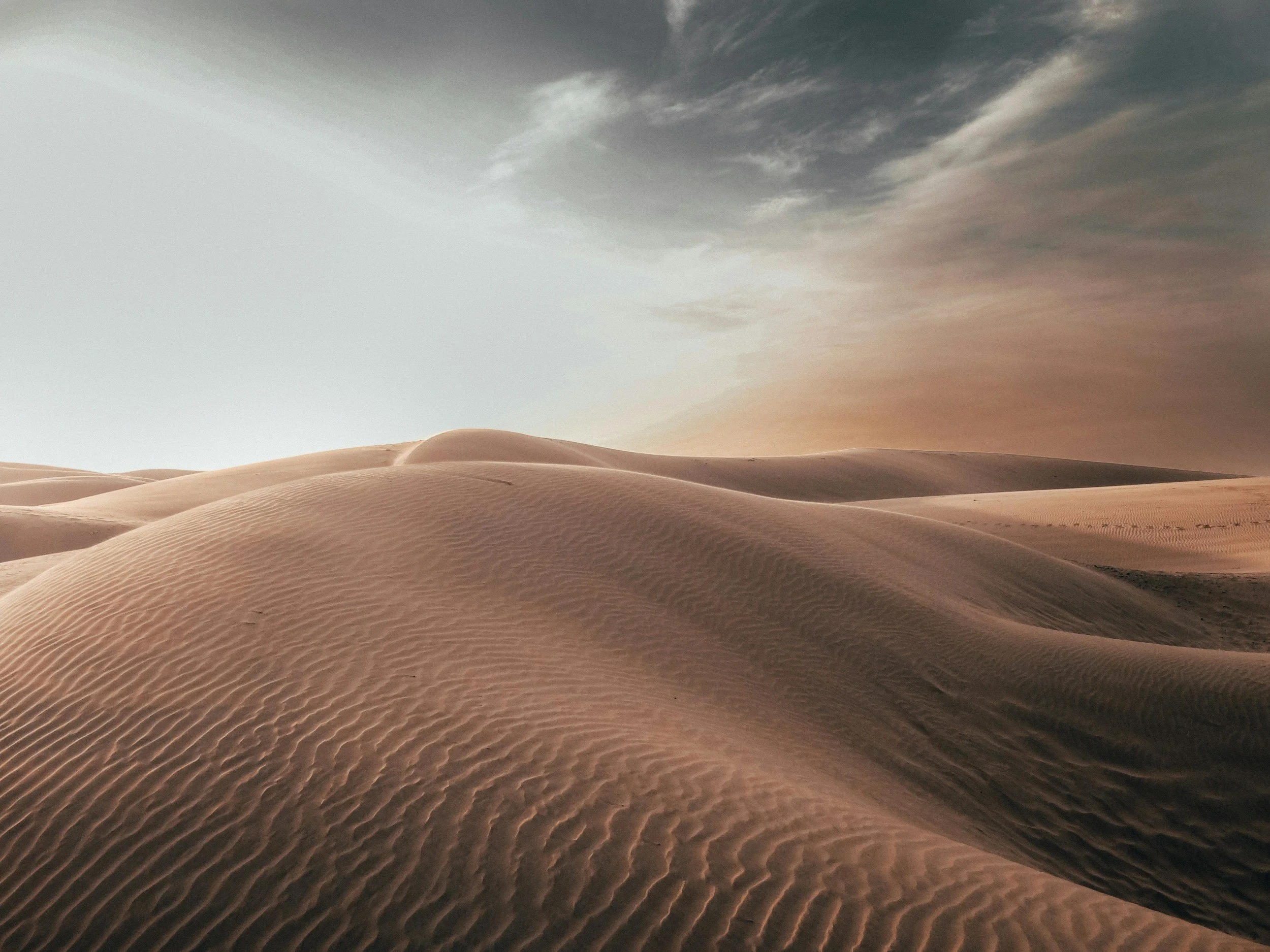 Sand dunes in a desert with a dark cloudy sky.