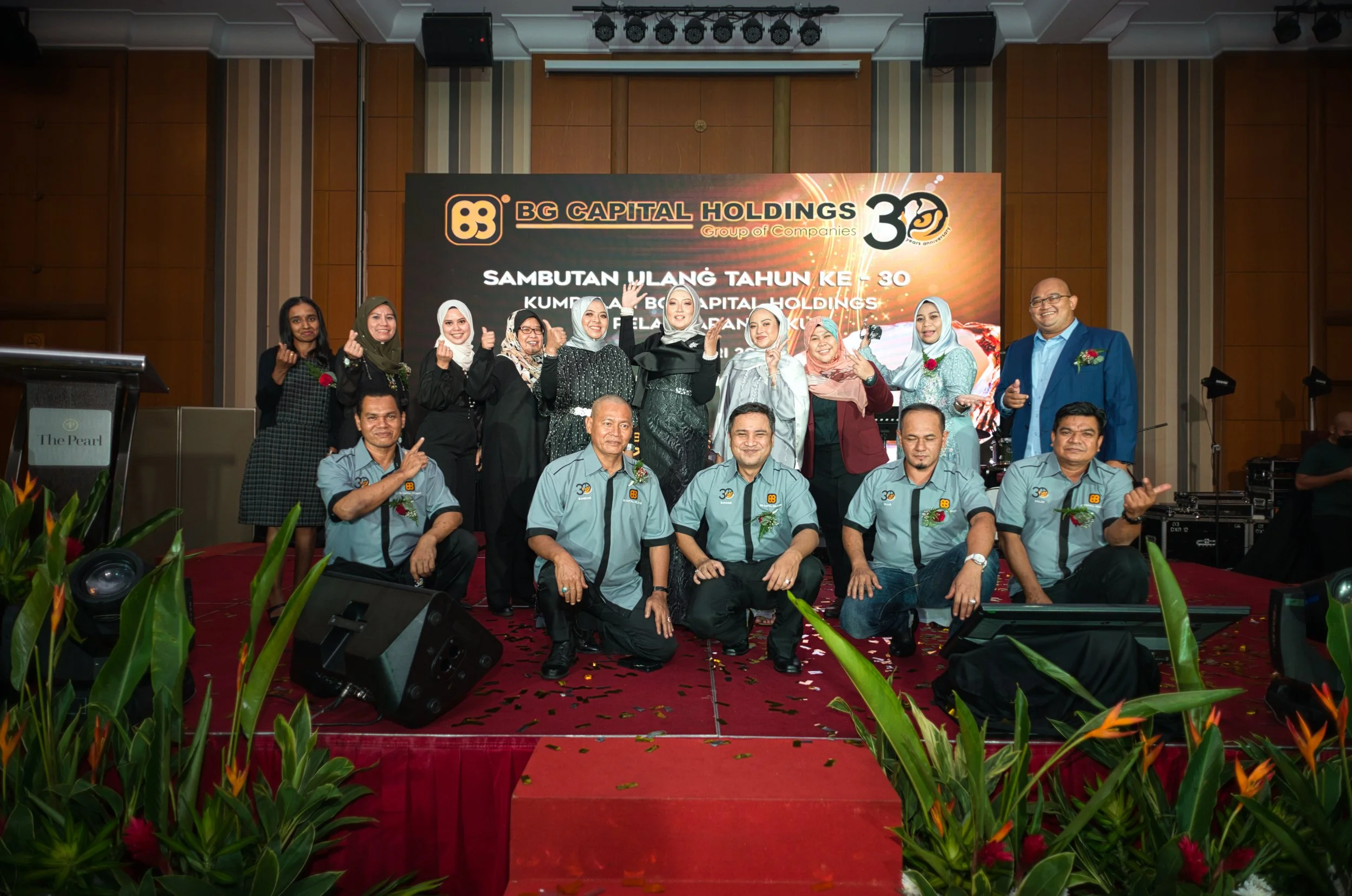 Group of people posing on stage at a celebration event for BG Capital Holdings' 30th anniversary, with a large banner in the background and decorations in the foreground.