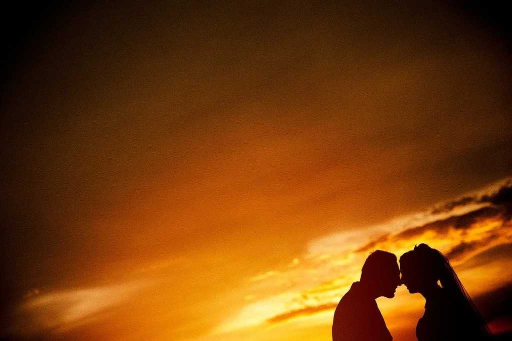 Silhouette of a bride and groom touching foreheads against a vibrant sunset sky.