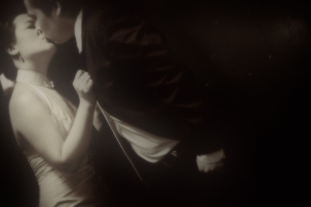 A black-and-white photograph of a couple sharing a kiss in a romantic setting, with the woman wearing a sleeveless dress.