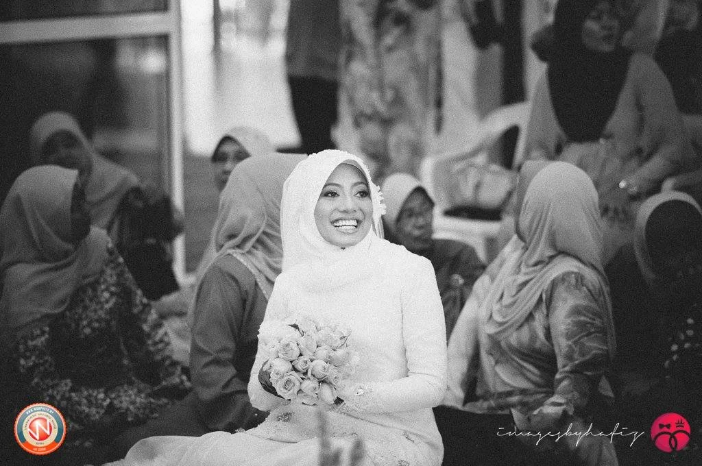 A smiling woman wearing a hijab holding a bouquet of flowers at a gathering with several women in hijabs around her