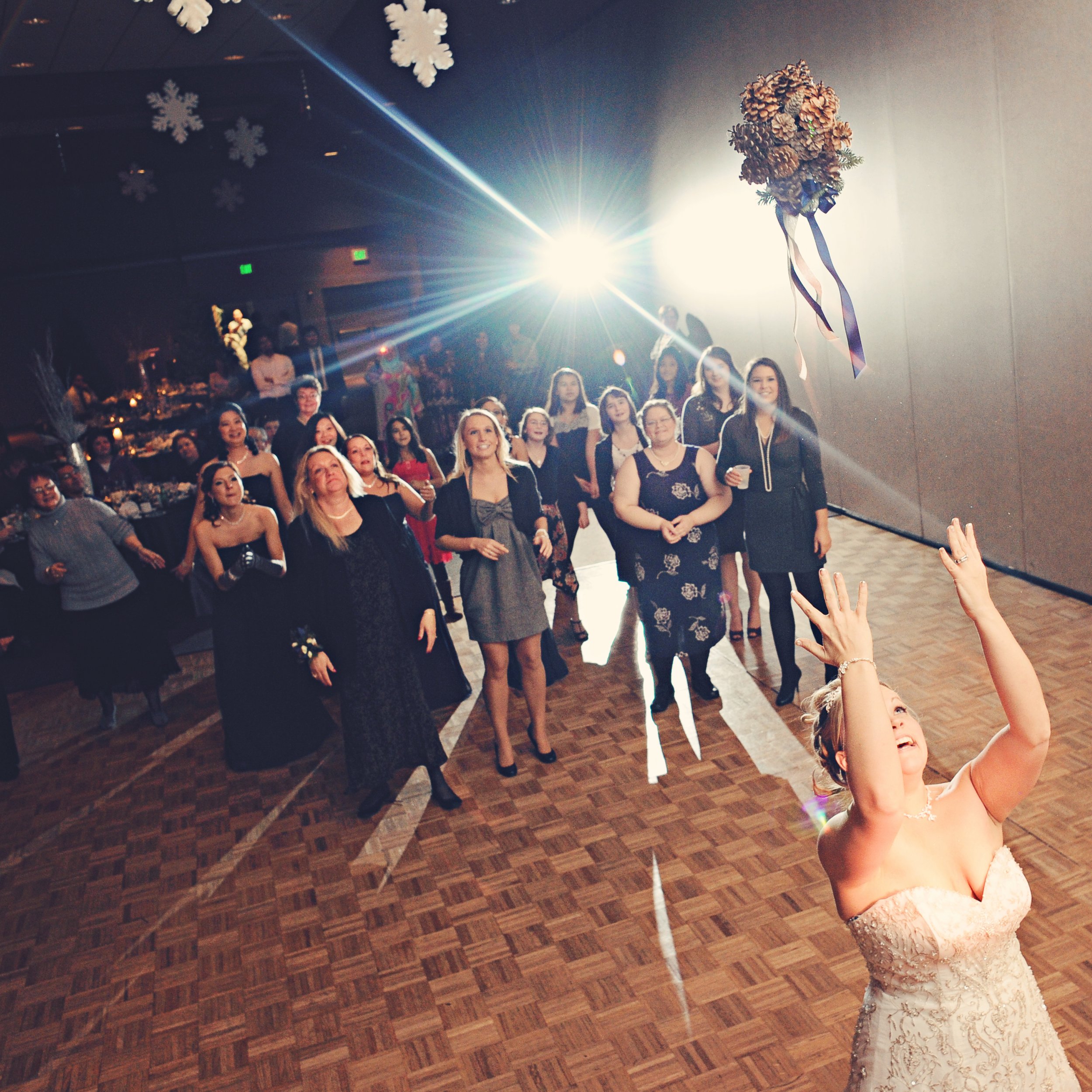 A woman in a wedding dress is tossing her bouquet to a group of women standing on the dance floor at a wedding reception.