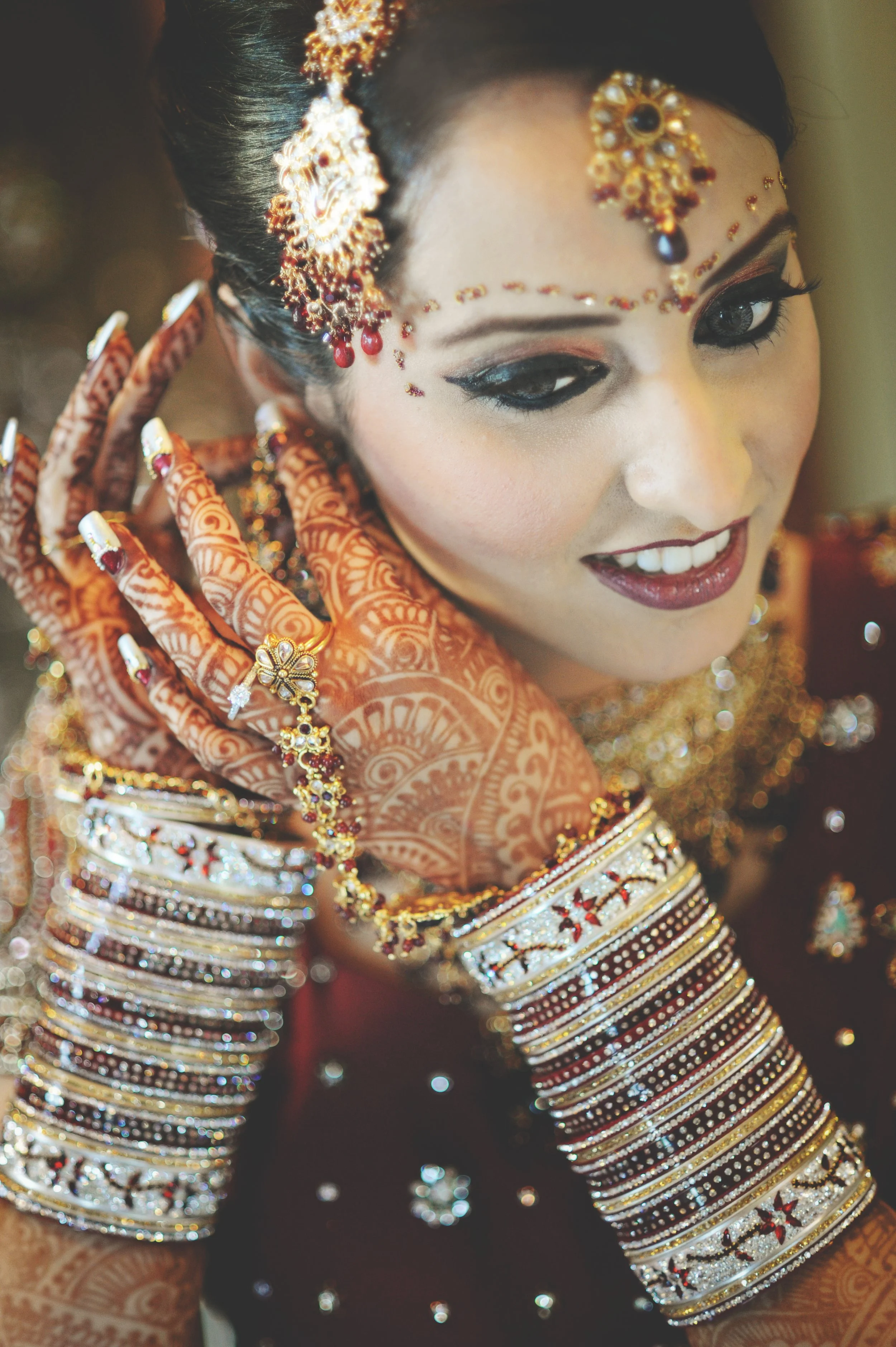 A woman dressed in traditional Indian bridal attire with bangles, jewelry, henna tattoos on her hand, and intricate makeup.