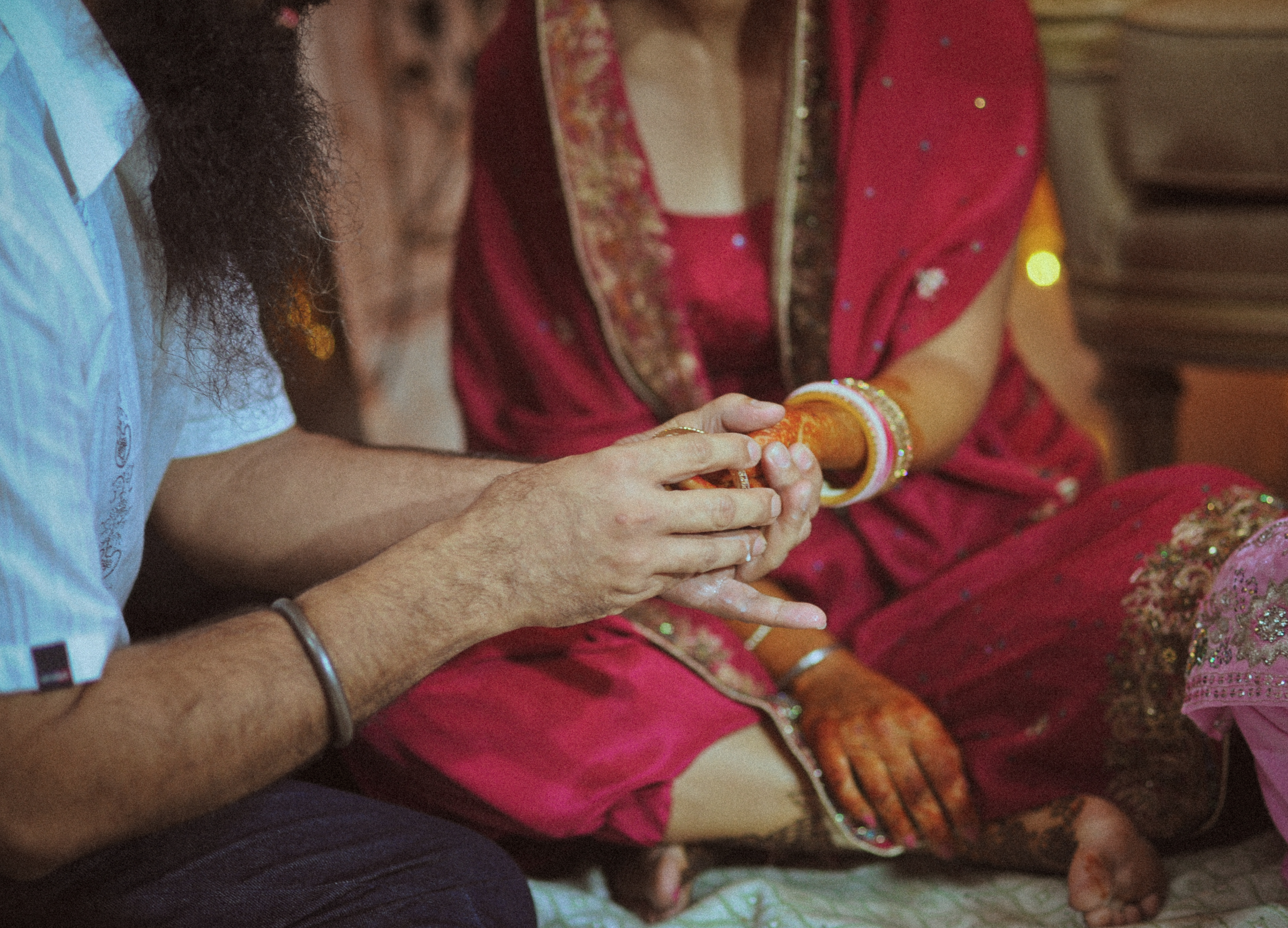 A person wearing a white shirt holding hands with a woman dressed in traditional Indian attire, adorned with jewelry and henna, during a cultural or religious ceremony.
