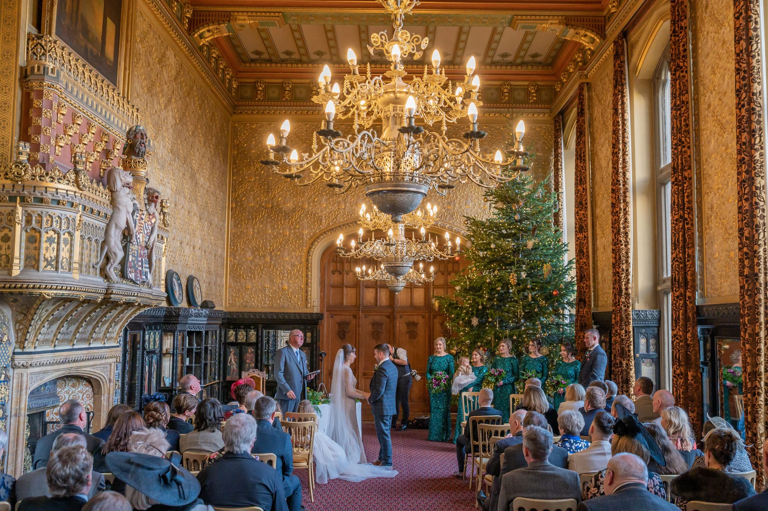 Couple getting married in the Venetian State Room at Christmas with a large Christmas Tree and Chandeliers casting a golden glow.