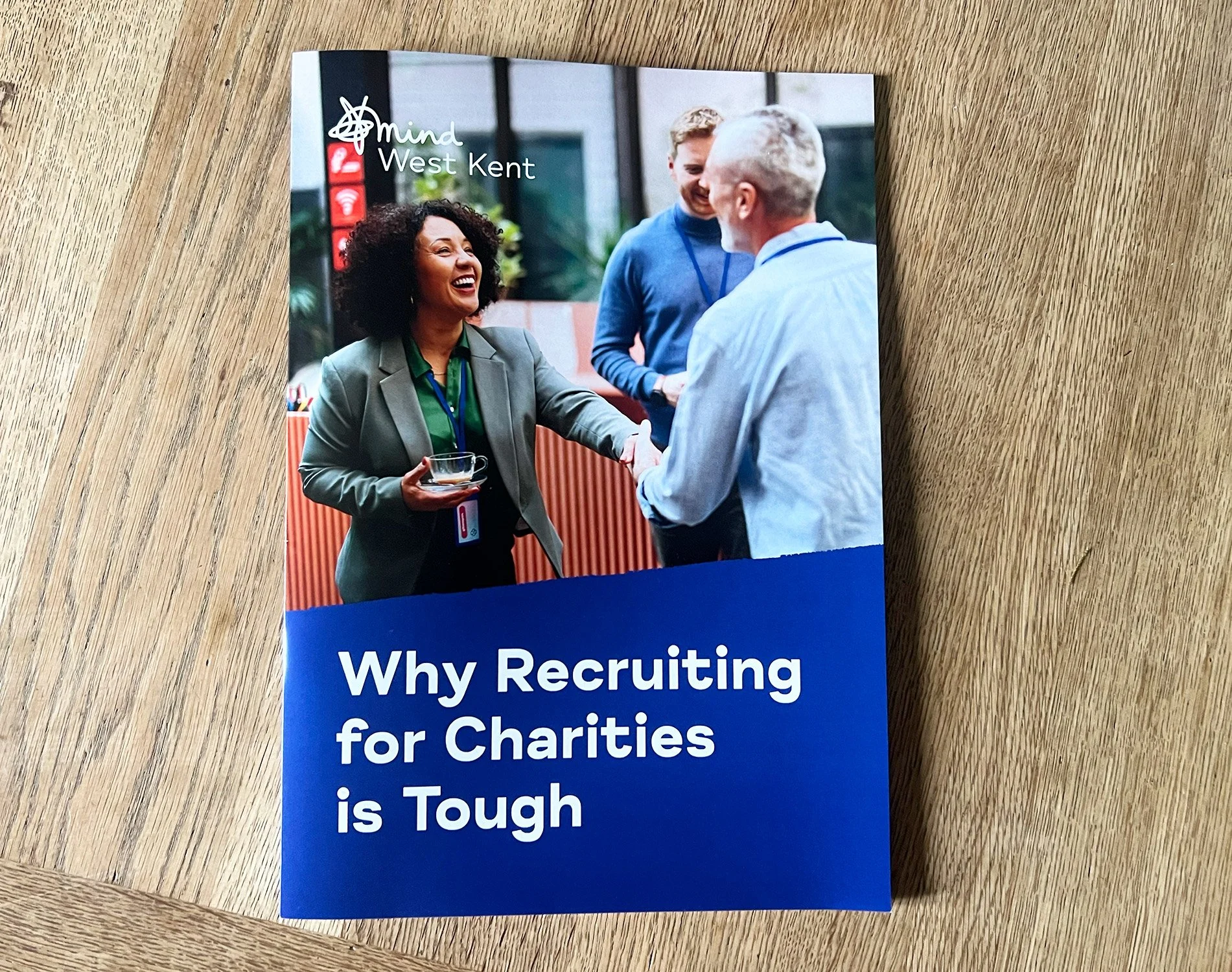 West Kent Mind 'Why Recruiting for Charities is Tough' brochure. Front cover has a bold Mind Brand Blue block and an image of a smiling lady shaking hands with a grey-haired man.
