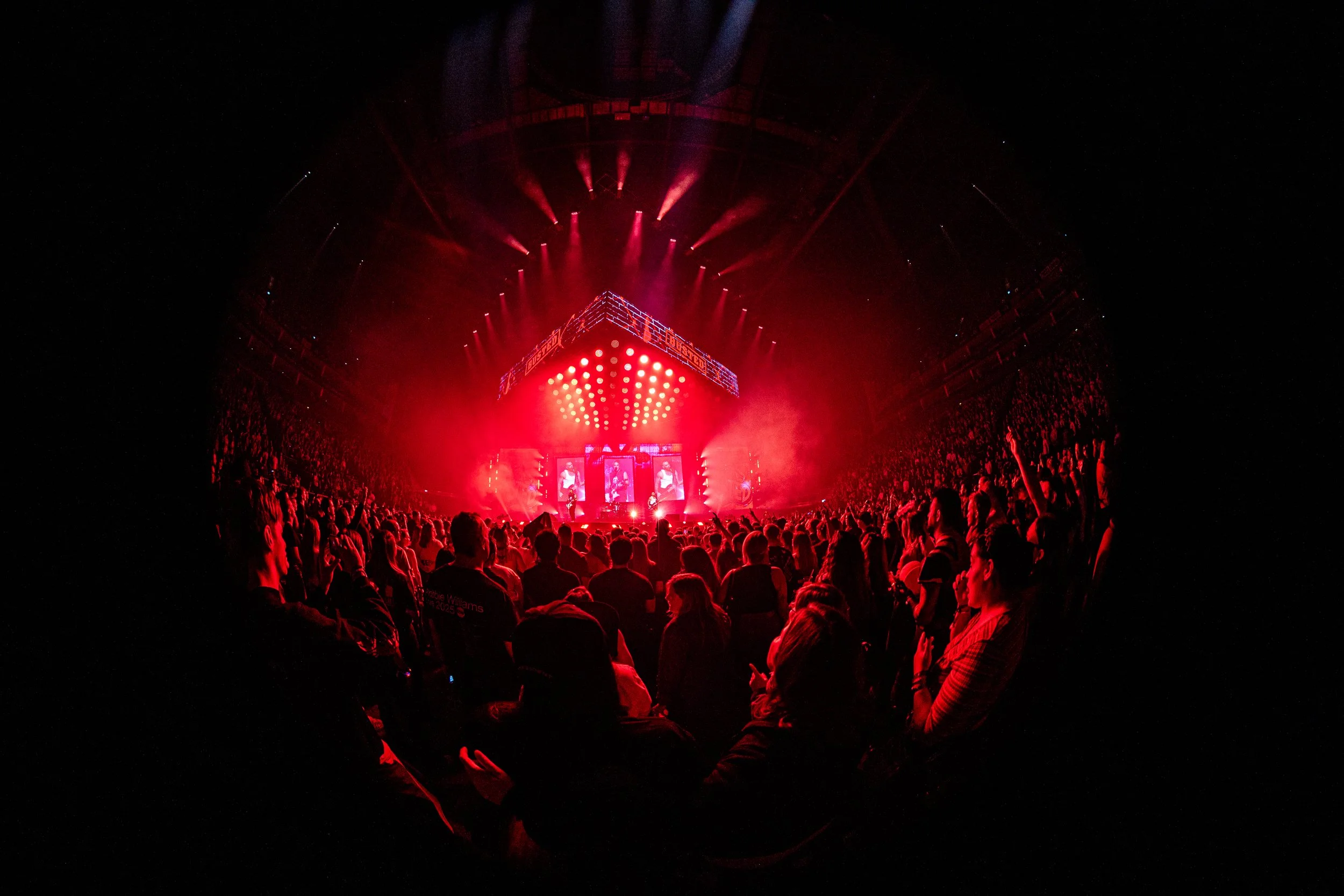 Crowd attending a concert or performance with red stage lights and visual displays.