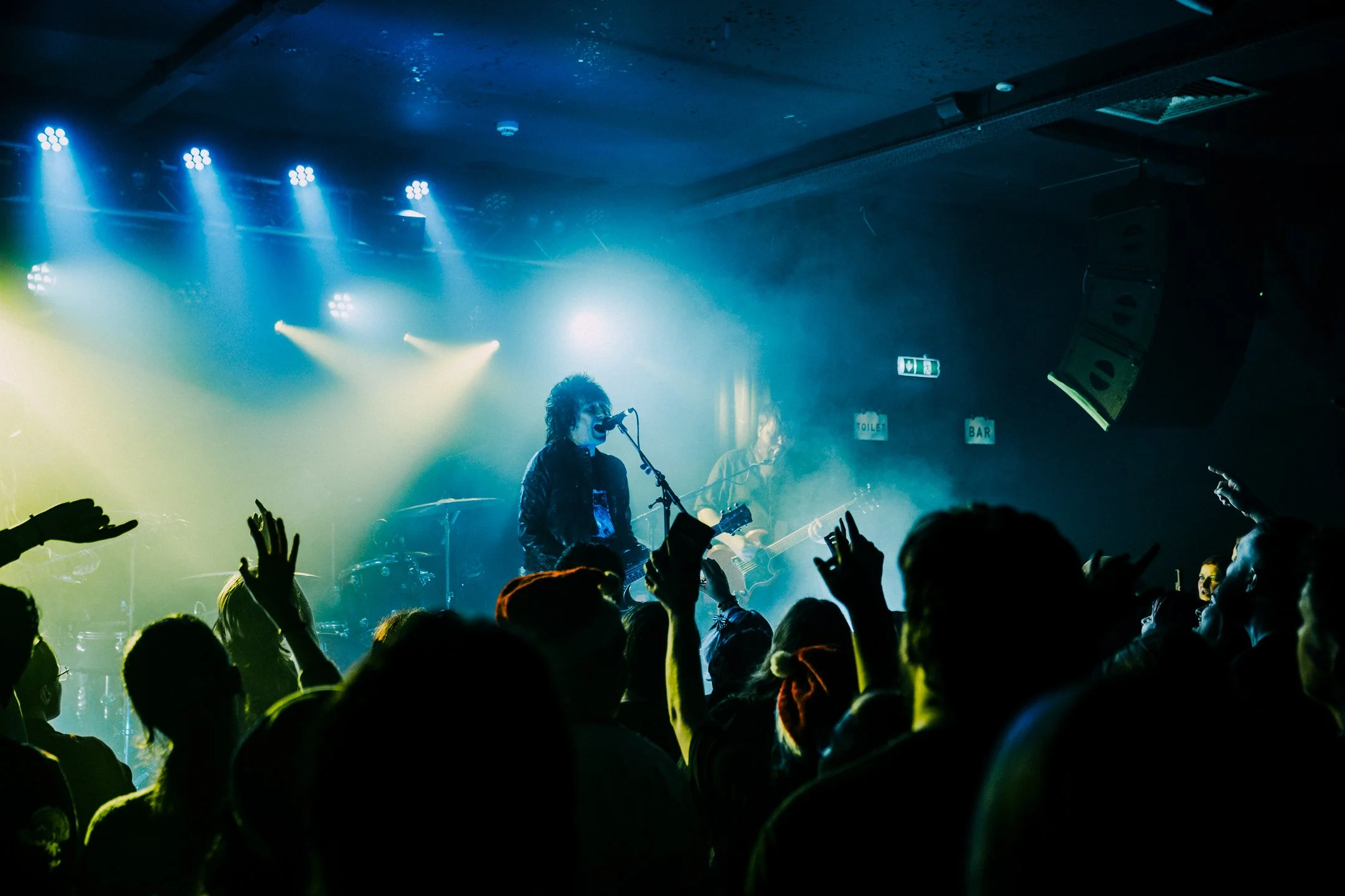 Live concert with musicians performing on stage, colorful lighting, and an audience raising their hands.