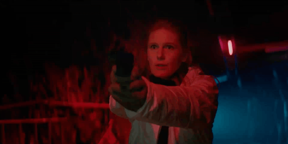 A woman with red hair aiming a gun, with red and blue neon lights in the background.