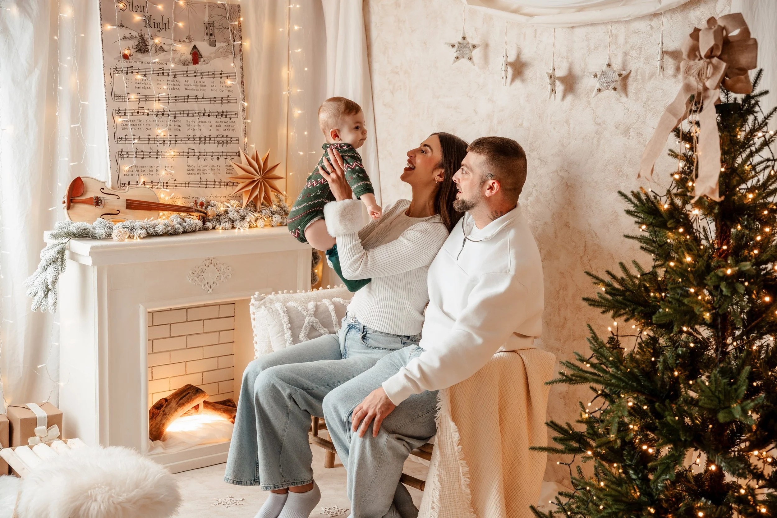 Familia en celebración navideña en sala decorada con árbol de Navidad iluminado, estrellas colgantes, y decoraciones blancas y doradas.