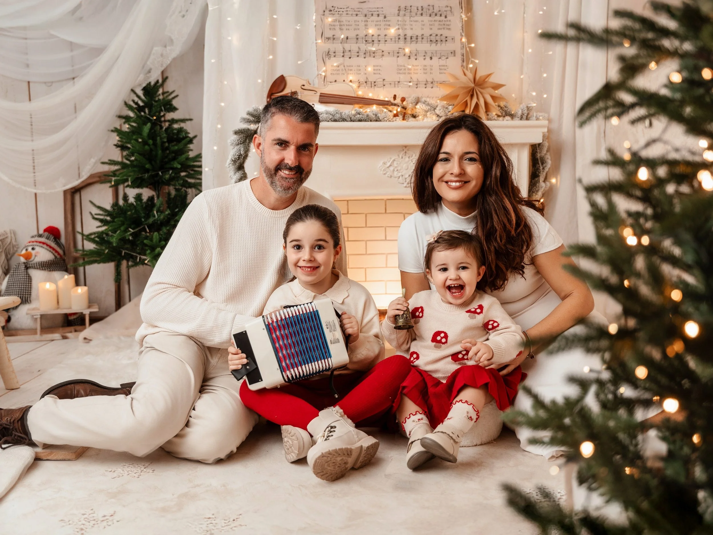 Una familia posando junta junto a la chimenea decorada con motivos navideños, rodeada de árboles de Navidad, luces y adornos en un ambiente cálido y festivo.