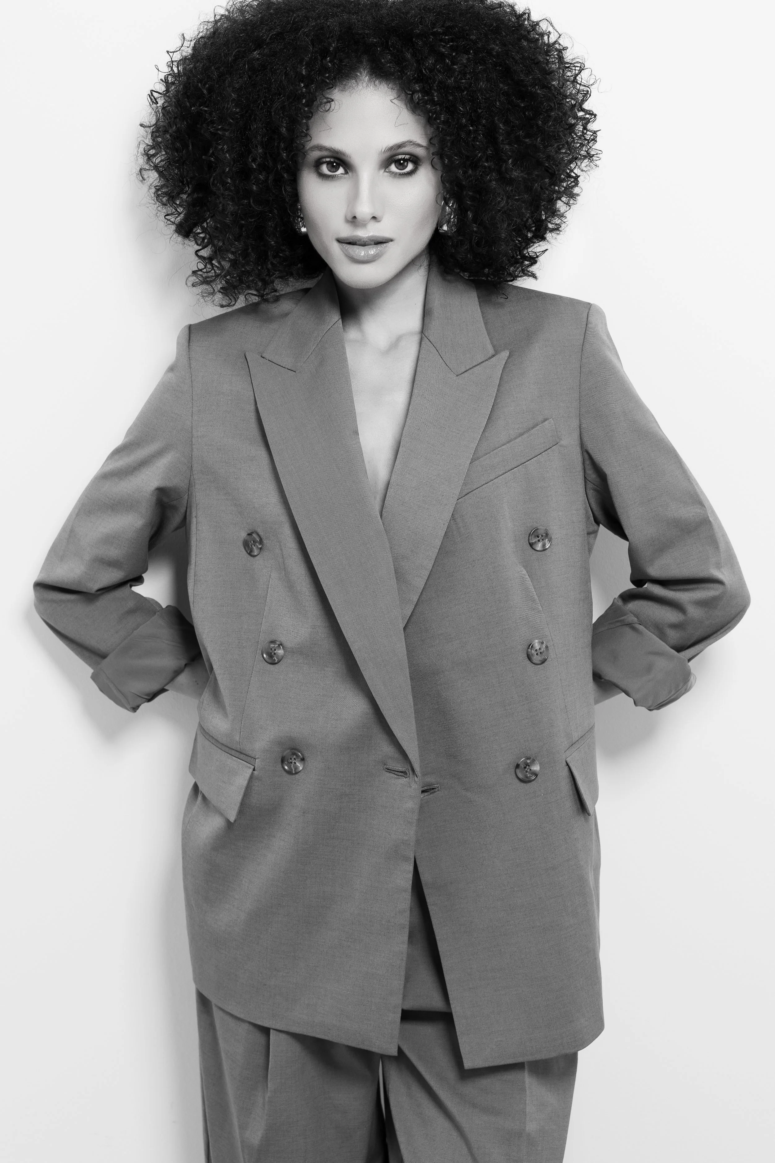 Schwarz-Weiß-Fotografie einer Frau mit lockigem Haar in einem Business-Anzug, die direkt in die Kamera schaut.