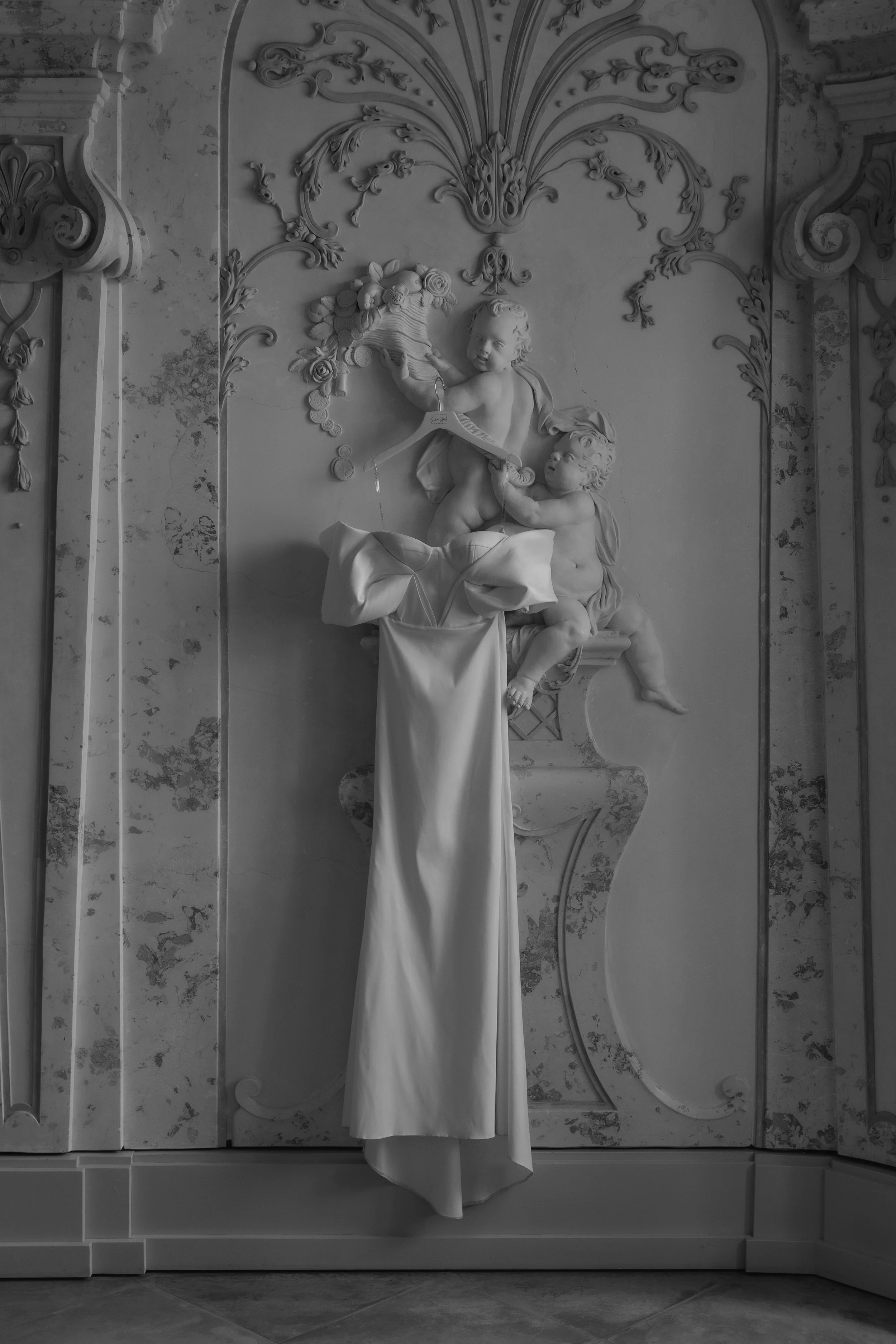 Ein barocker Wandrelief mit zwei Akteuren, einem Engel mit Flügeln und einem Kind, das auf einer Säule sitzt, mit einem Buch in der Hand.