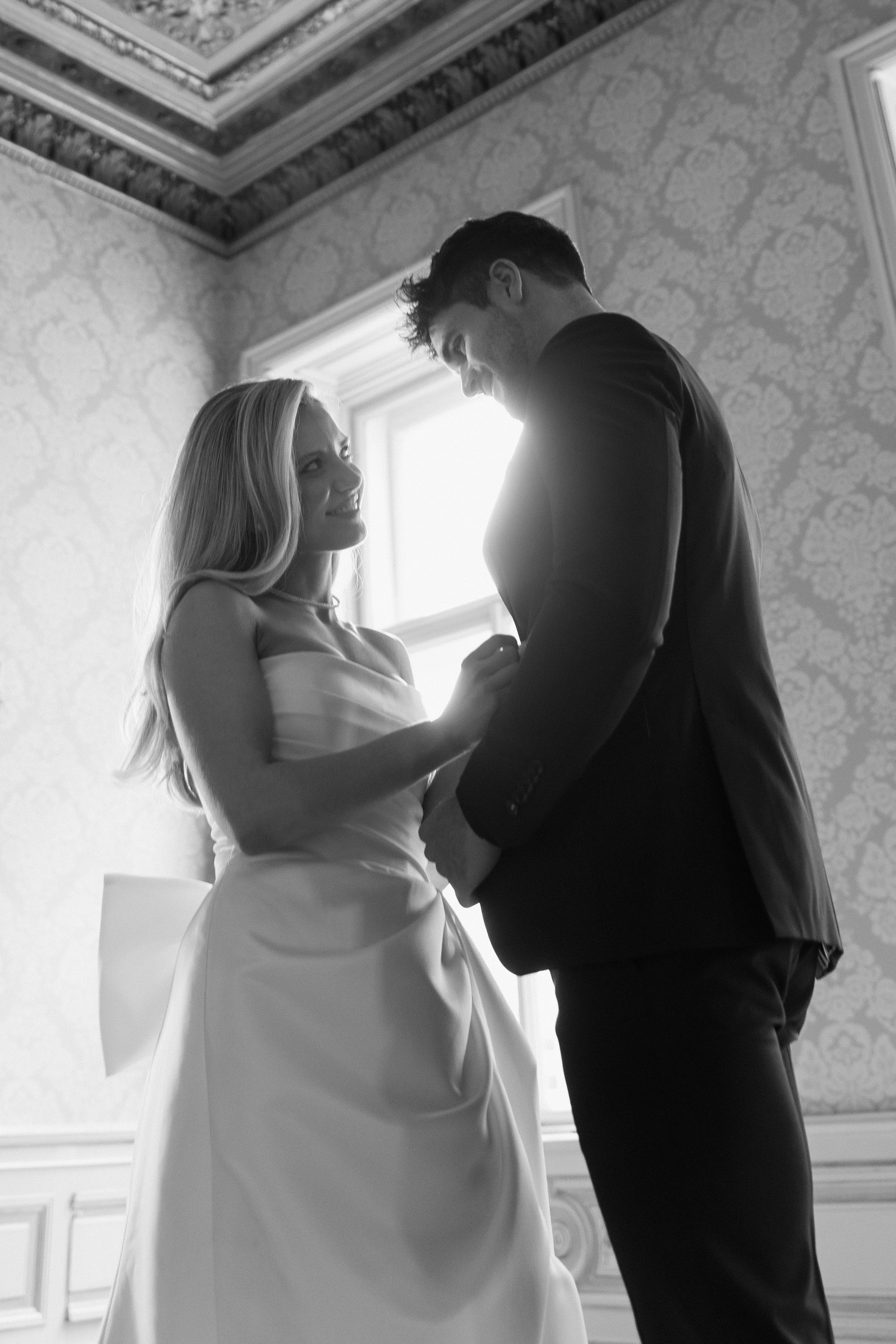 Braut und Bräutigam während ihrer Hochzeitszeremonie, im Schwarz-Weiß-Stil, vor einem Fenster, im eleganten Raum mit dekoriertem Decke.