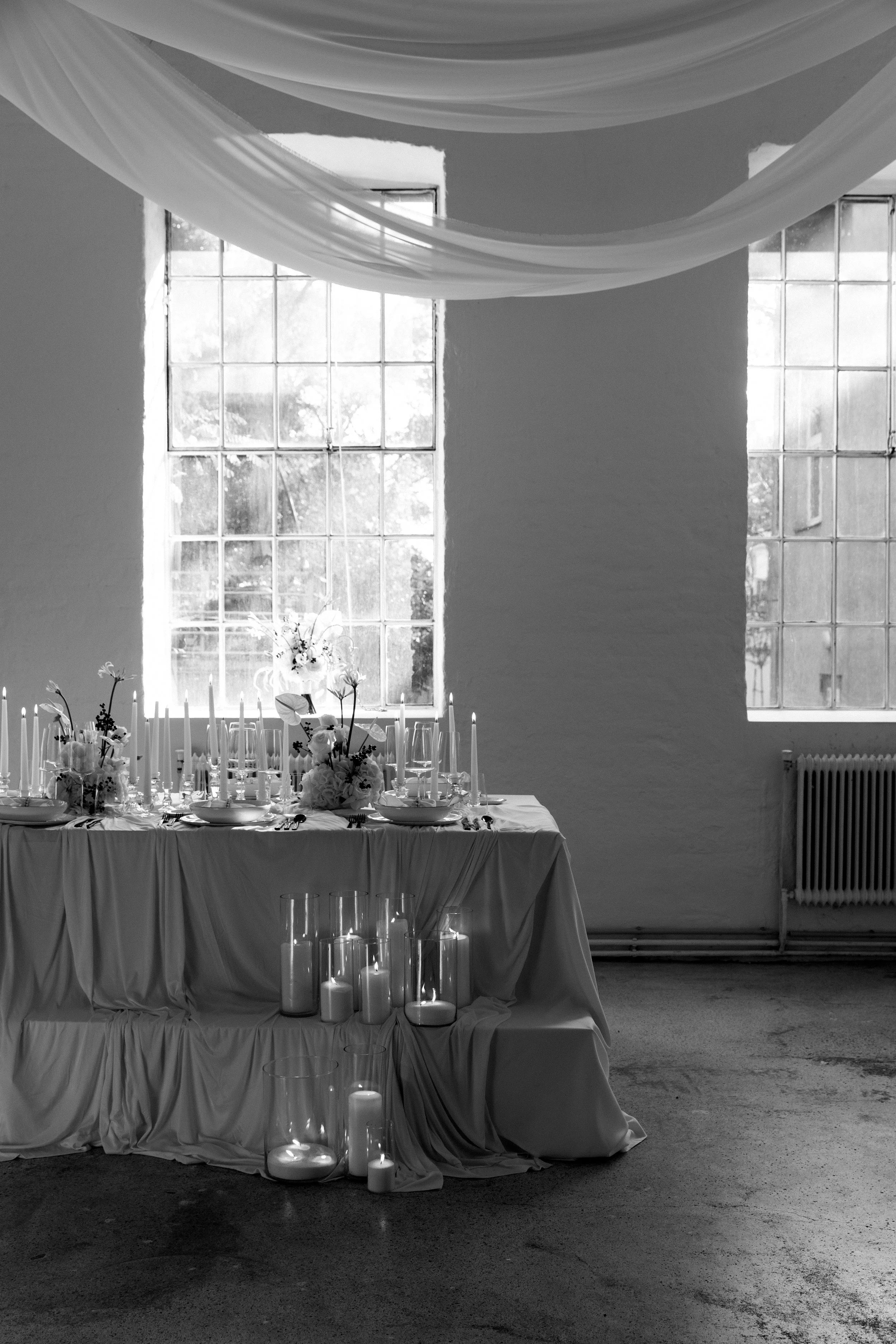 Ein festlich gedeckter Esstisch mit Blumen, Kerzen und Geschirr vor einem Fenster. 