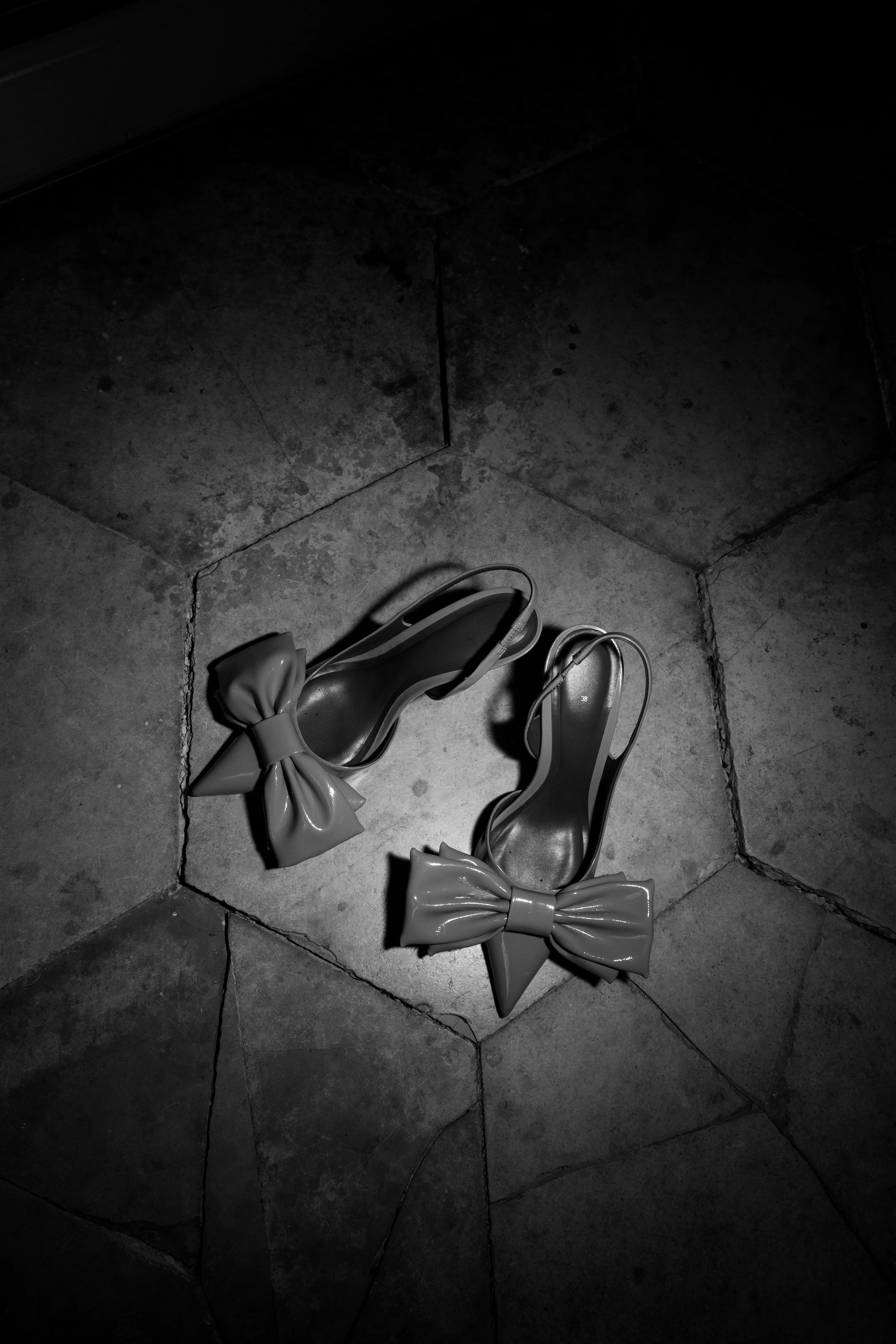 Zwei high heels Schuhpaare mit großen Schleifen, die auf einem Fliesenboden liegen, schwarz-weiß