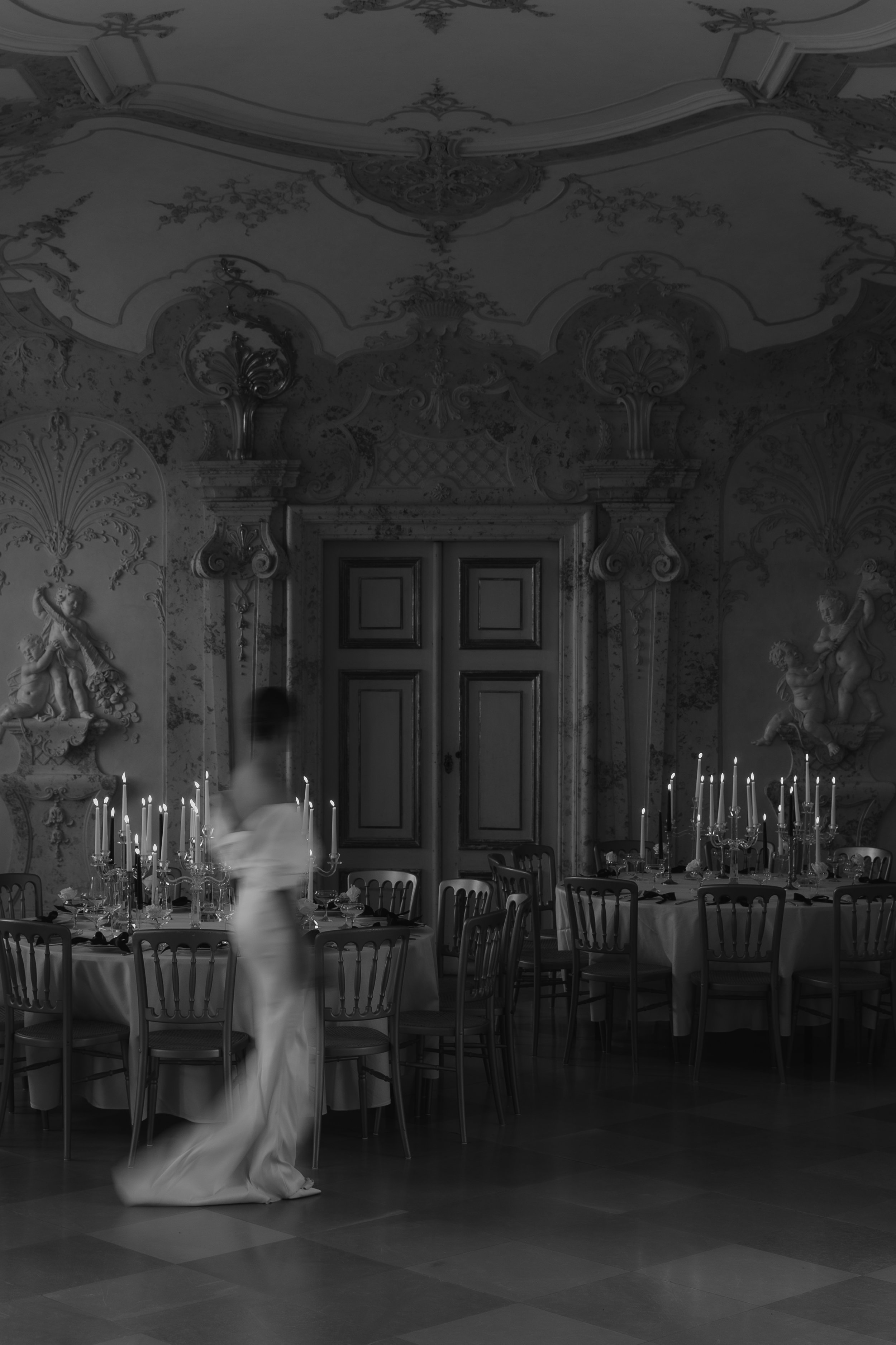 Ein eleganter, historischer Speisesaal mit gedecktem Tisch, Kerzenleuchtern, Wandreliefs und einem Mädchen in einem langen Kleid, das durch den Raum geht.