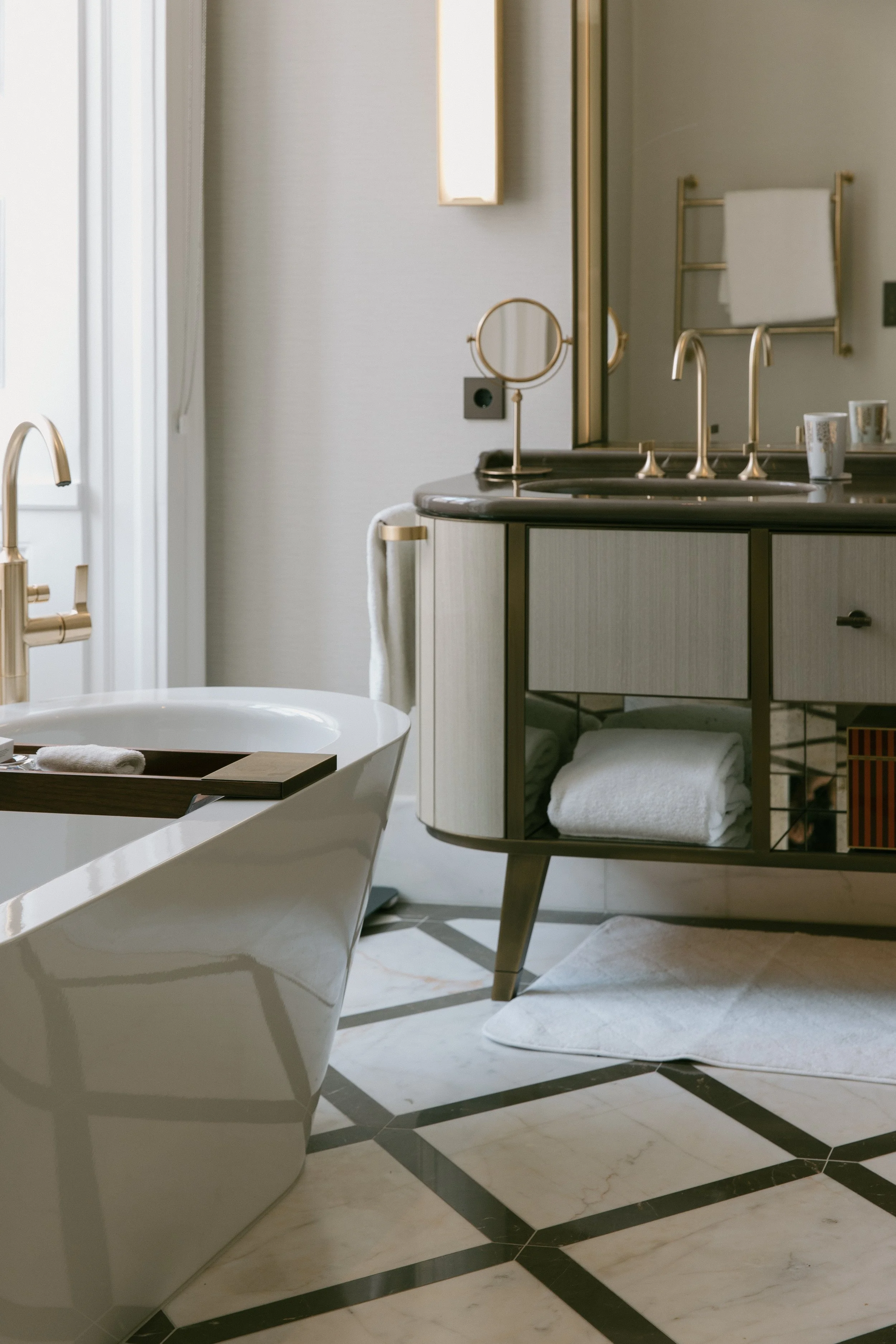 Elegantes Badezimmer mit freistehender Badewanne, moderner Waschtisch mit goldenen Armaturen, Spiegel und Handtuchhalter.