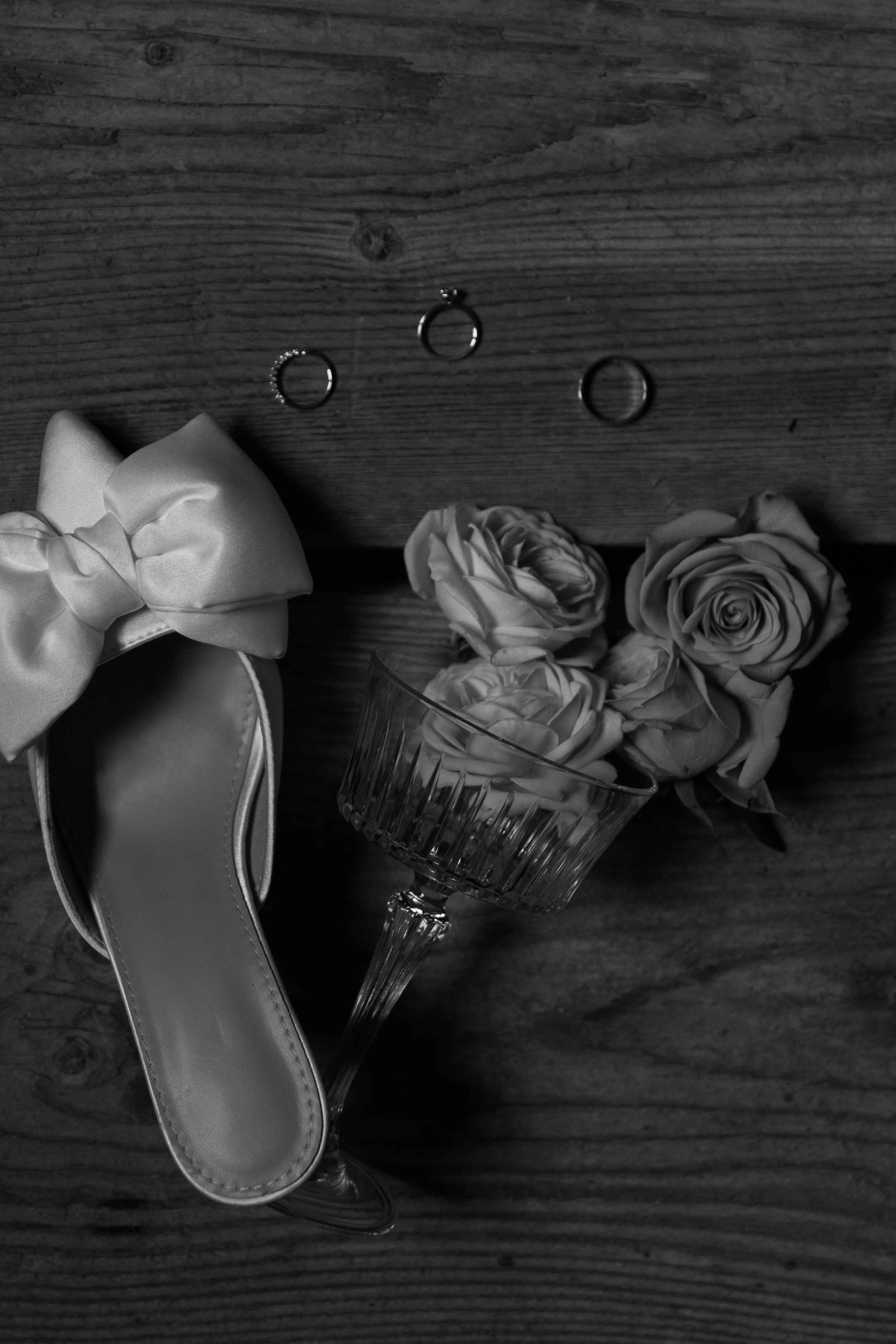 Schmuck, Blumen und ein Schuh auf einem Holztisch, in Schwarz-Weiß-Fotografie.