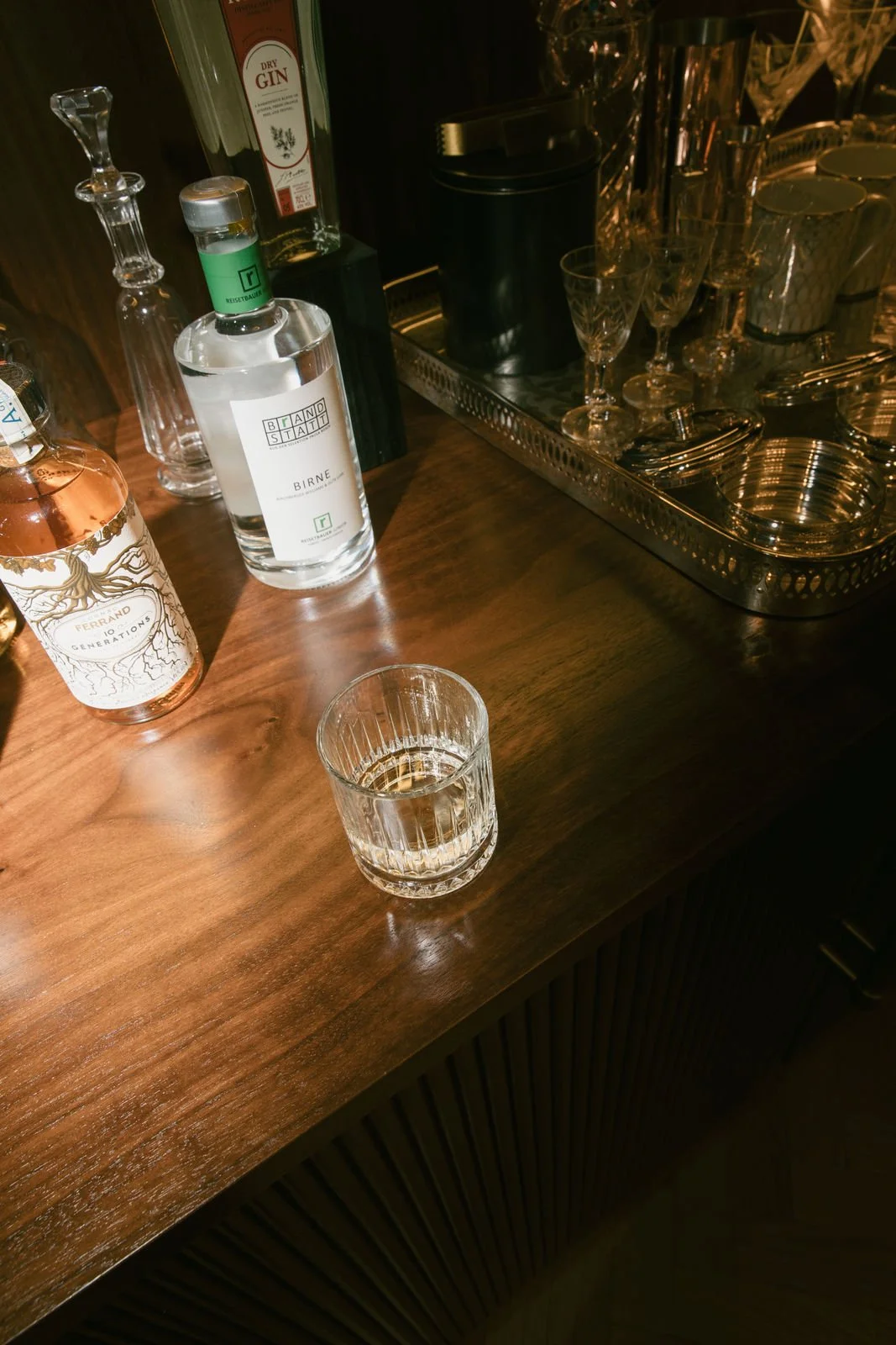 Flasche Gin, Flasche Birnenbrand, Glas mit Getränk, Kristallgläser, Tablett mit Barzubehör auf Holztisch.