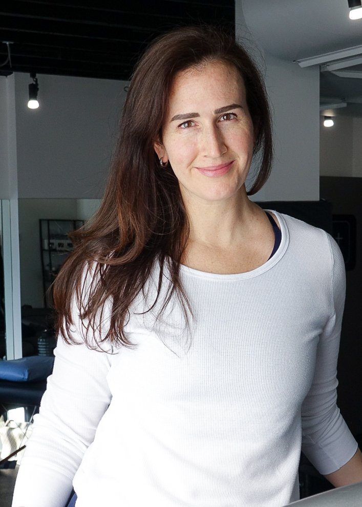 A woman with long brown hair smiling and looking at the camera.