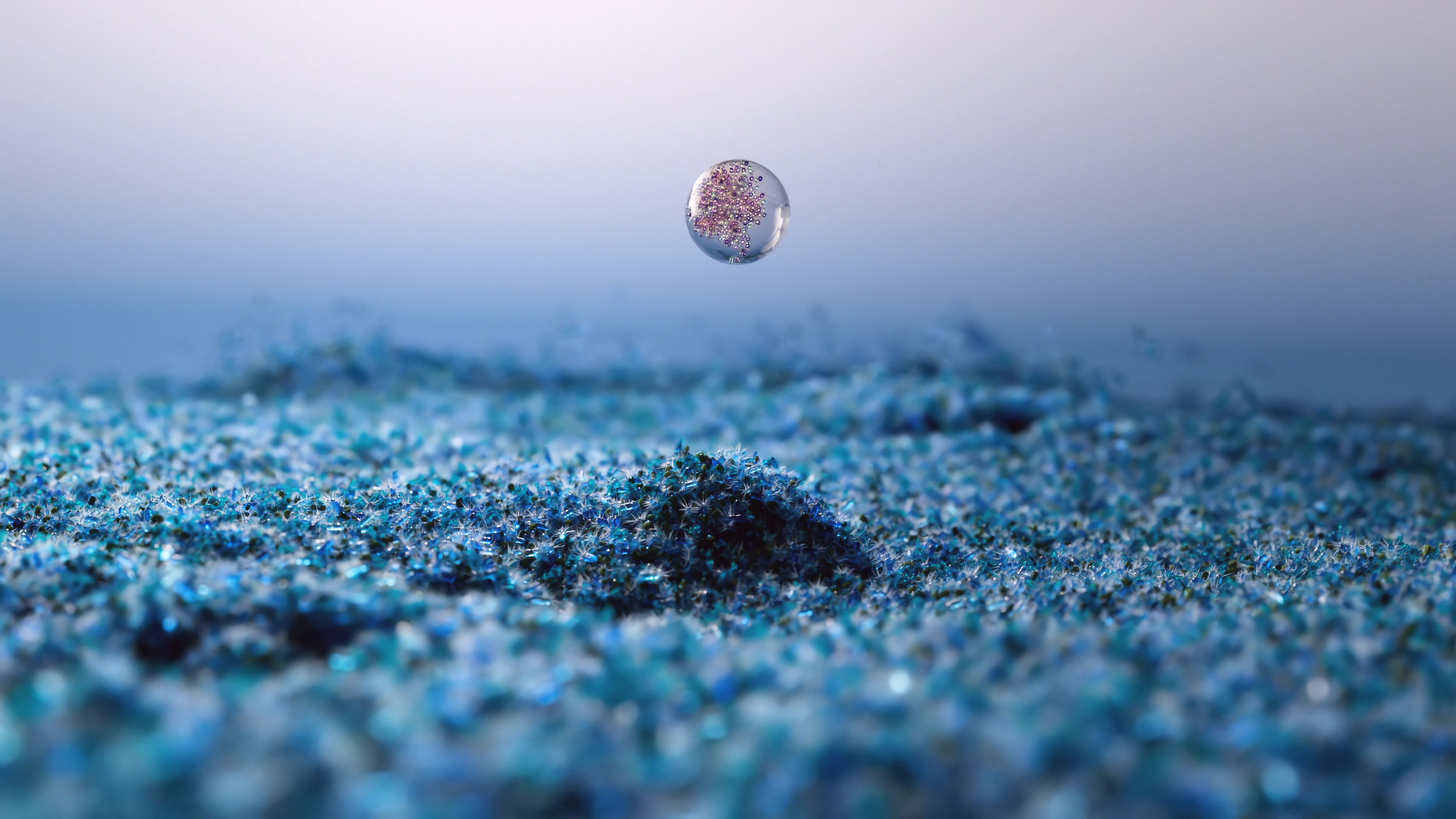 Small droplet suspended over a textured, blue surface with sparkles.