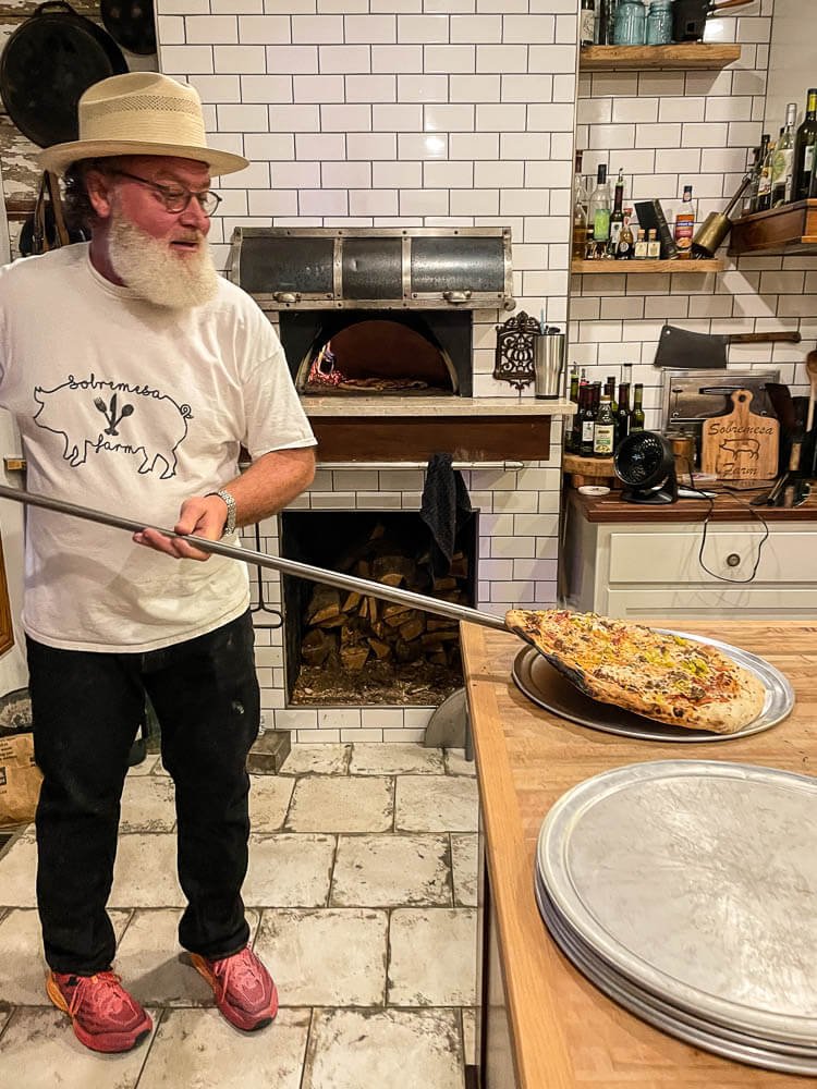 chef Ty pulling pizza from the brick oven at Sobremesa Farm Kitchen fine dining non profit restaurant