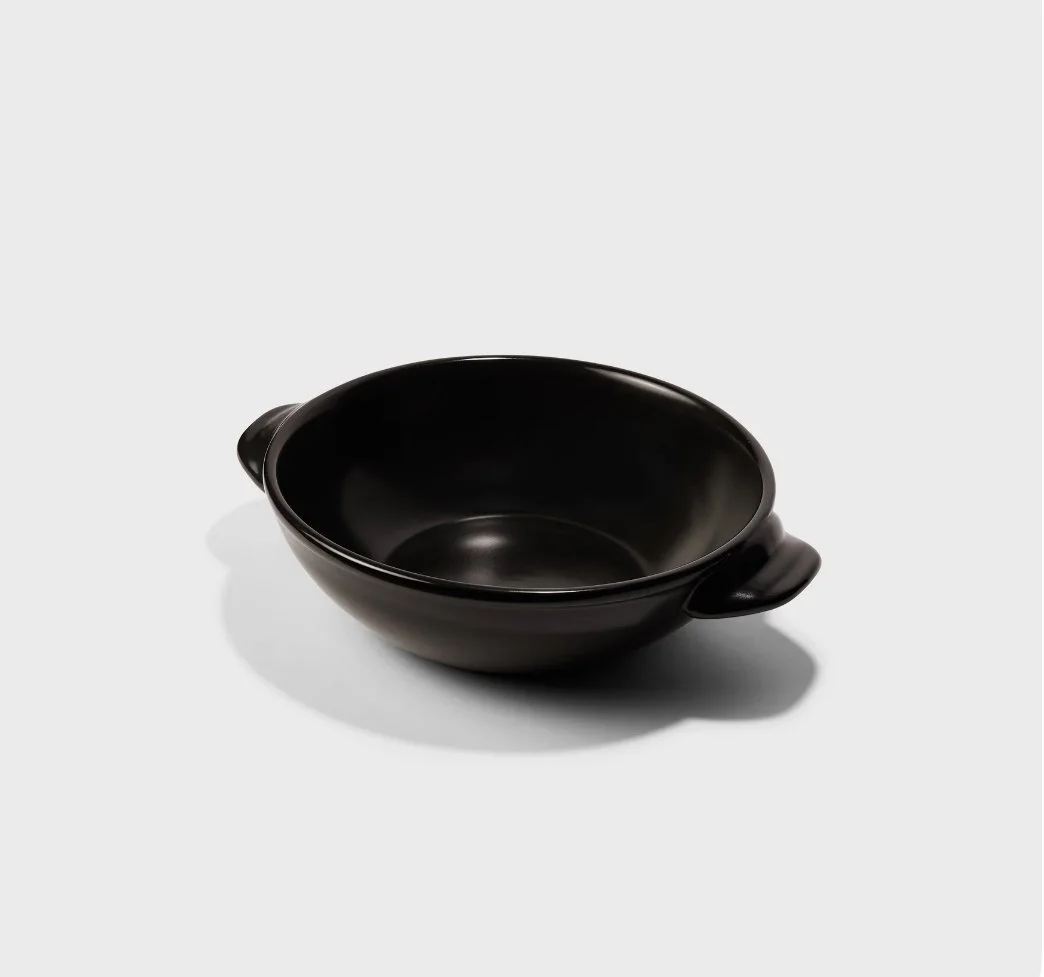 A black ceramic bowl with two small handles on a white background.