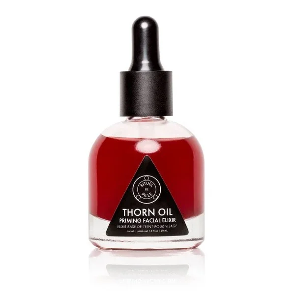 A glass bottle with a black dropper cap containing red liquid, labeled 'Thorn Oil Priming Facial Elixir' with a black triangle design.