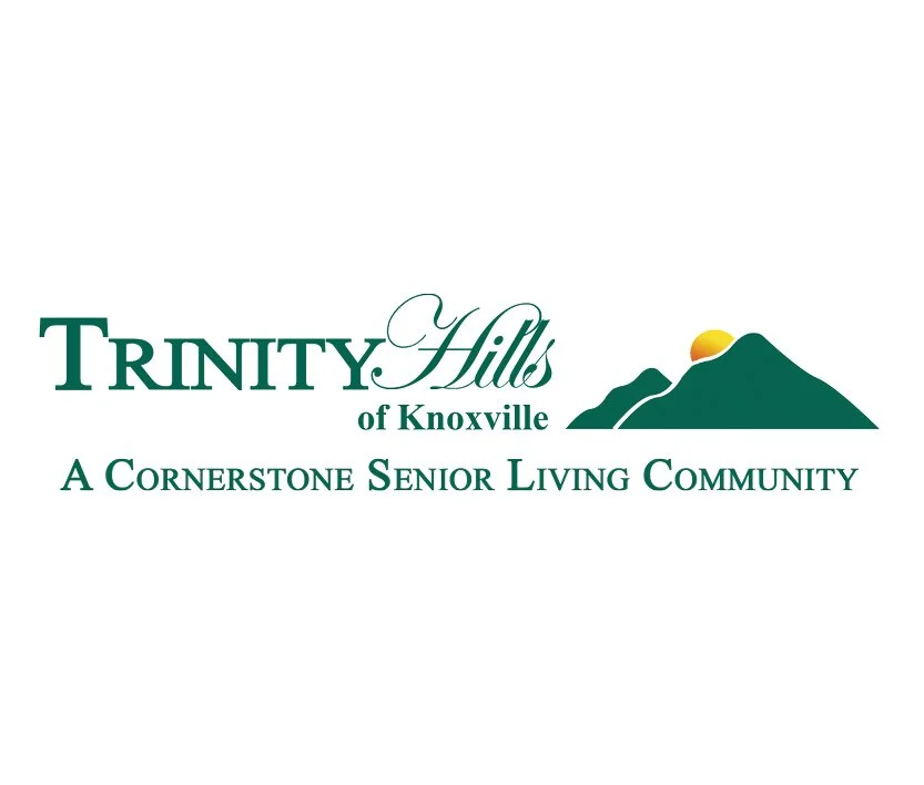 Logo for Trinity Hills of Knoxville, a cornerstone senior living community, featuring stylized green mountains with a sunrise behind them.