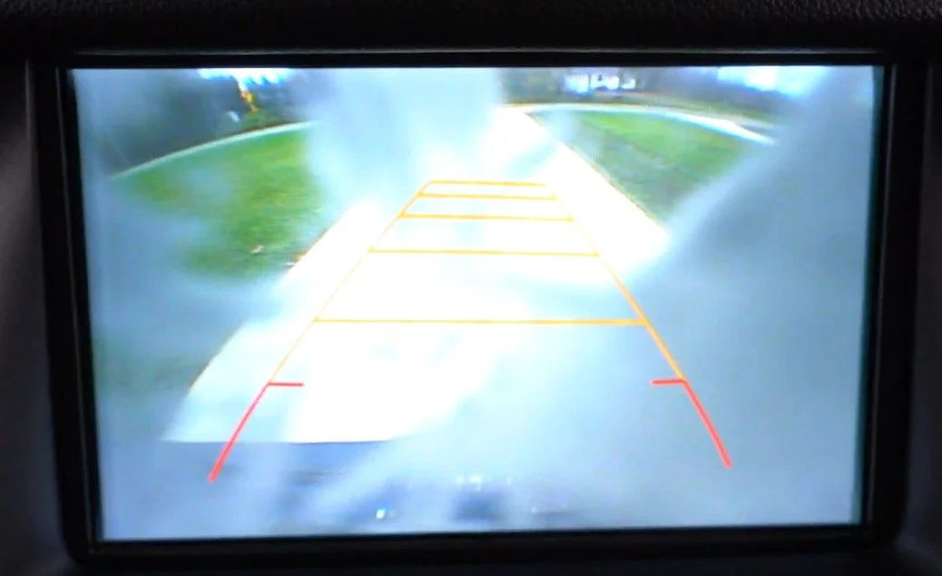 Car's backup camera displaying a wet parking lot with yellow and red guide lines.