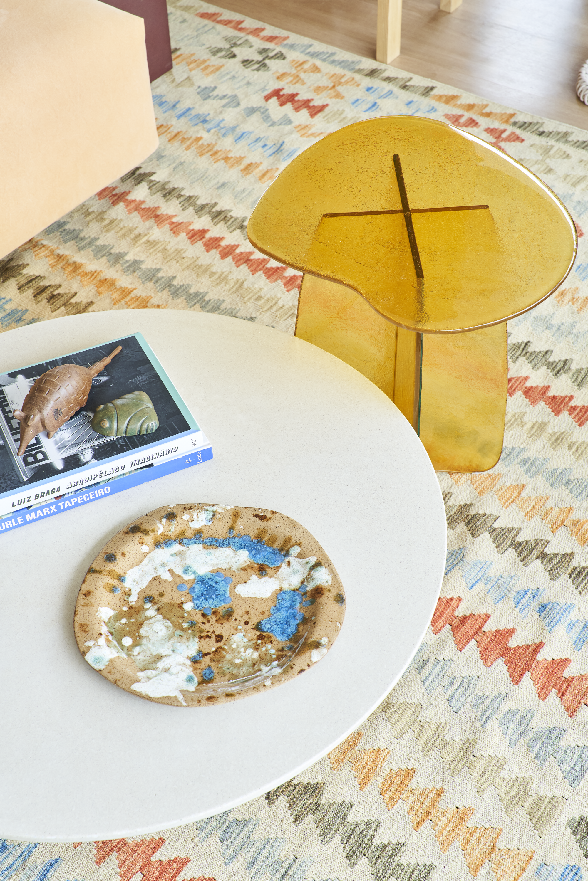 Vaso amarelo e mesa com livros, pratos decorativos e uma placa de vidro.