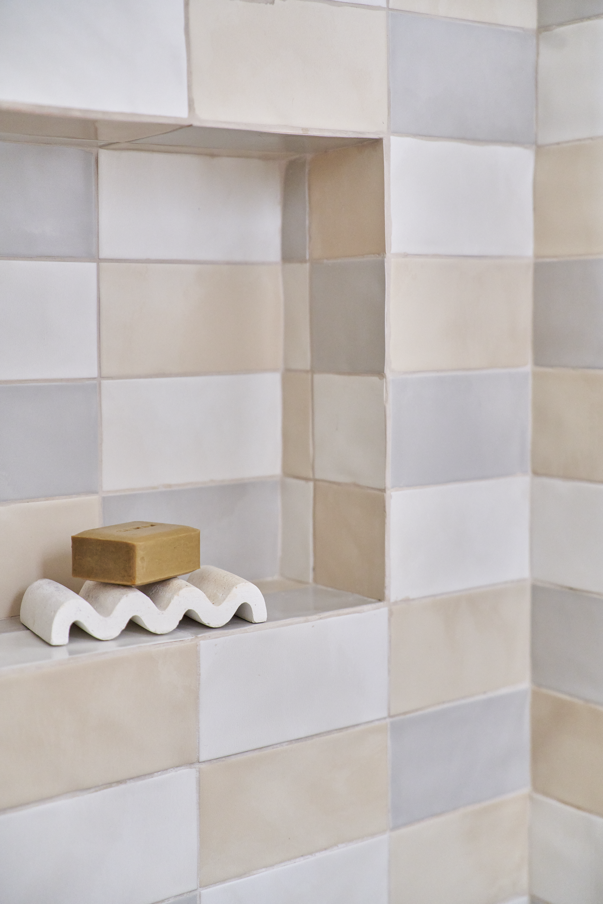 Tijolos decorativos em tons neutros na parede de um banheiro, com uma saboneteira branca segurando um sabonete marrom