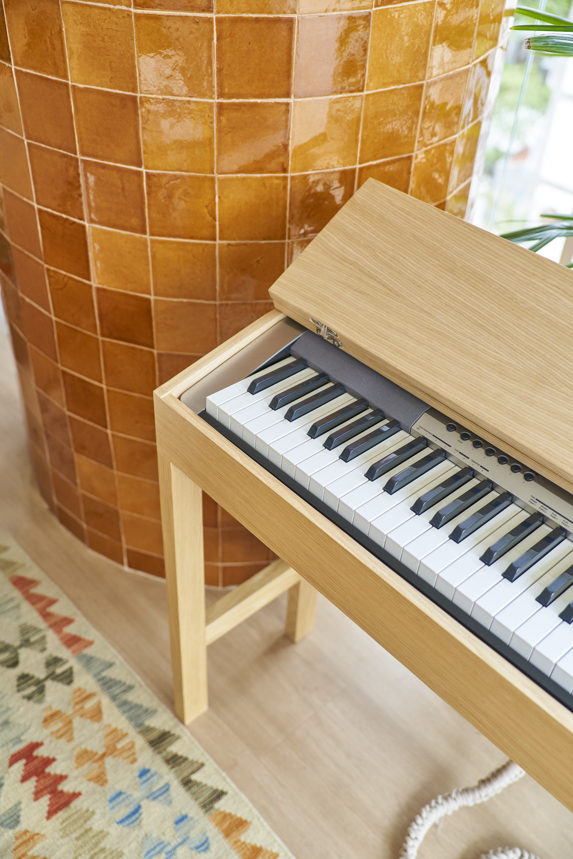 Piano de madeira claro ao lado de uma parede de azulejos laranja, com parte de um tapete colorido na parte inferior.