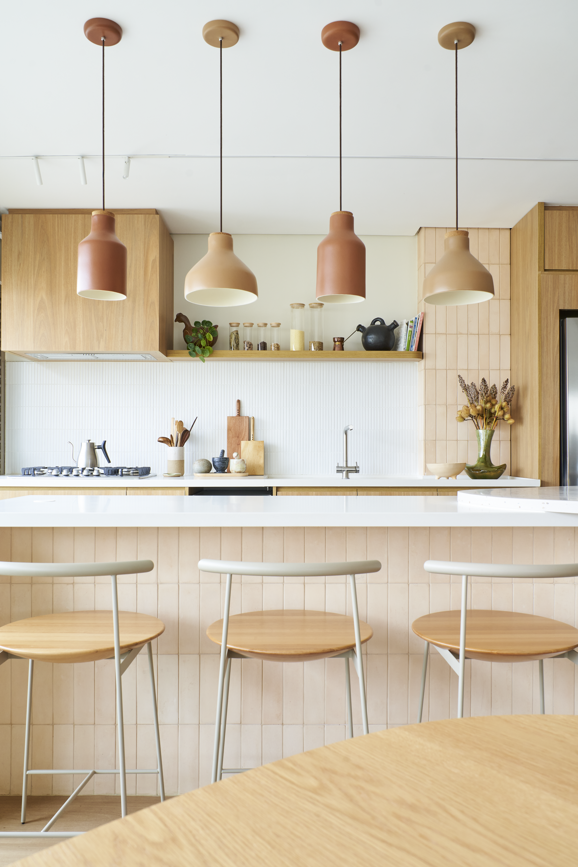 Cozinha com iluminação moderna, cadeiras de madeira e utensílios de cozinha decorativos na bancada