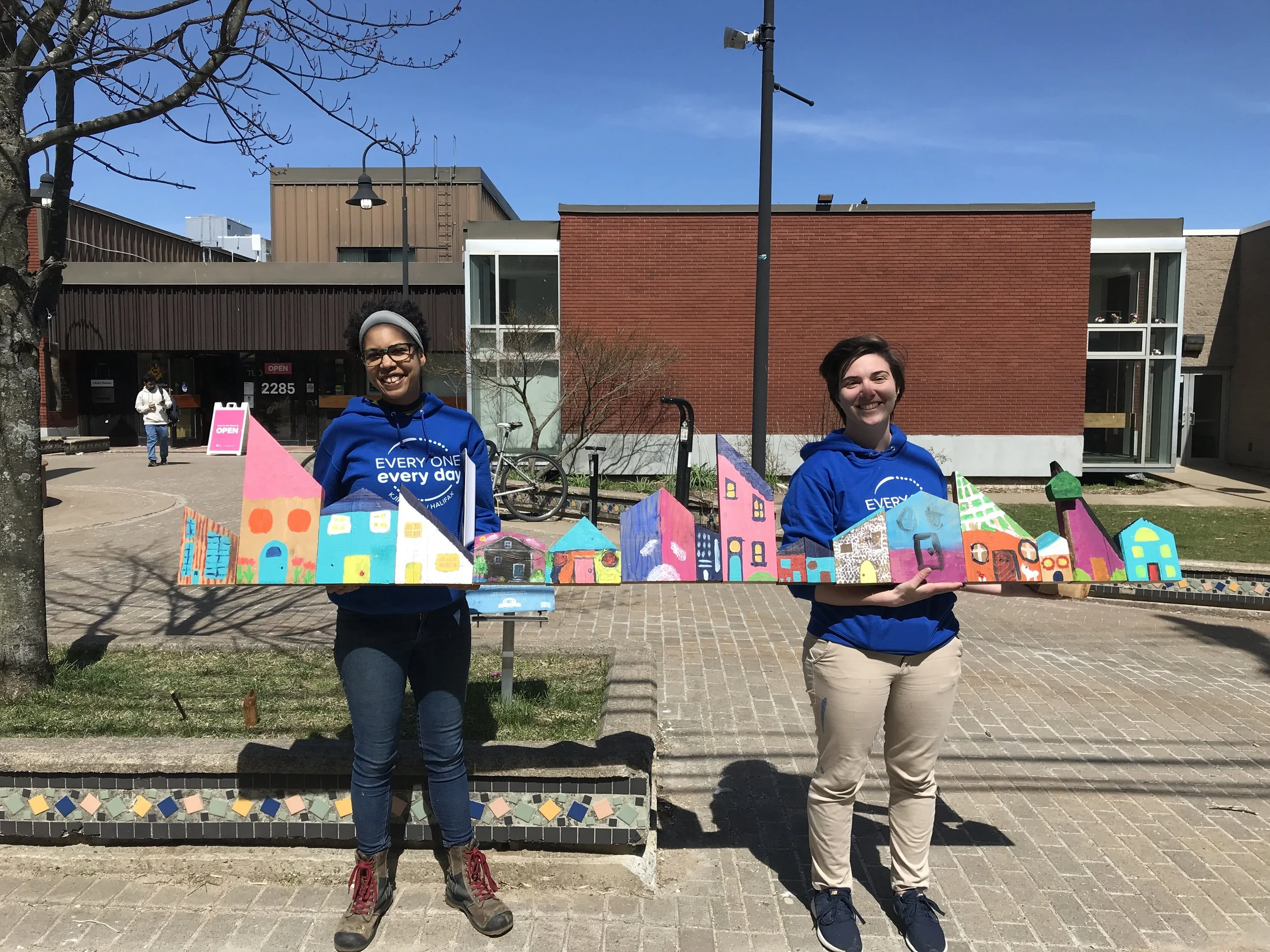 Kate and Adria pose with wooden houses made by community outside Halifax North Memorial Library, Spring 2023