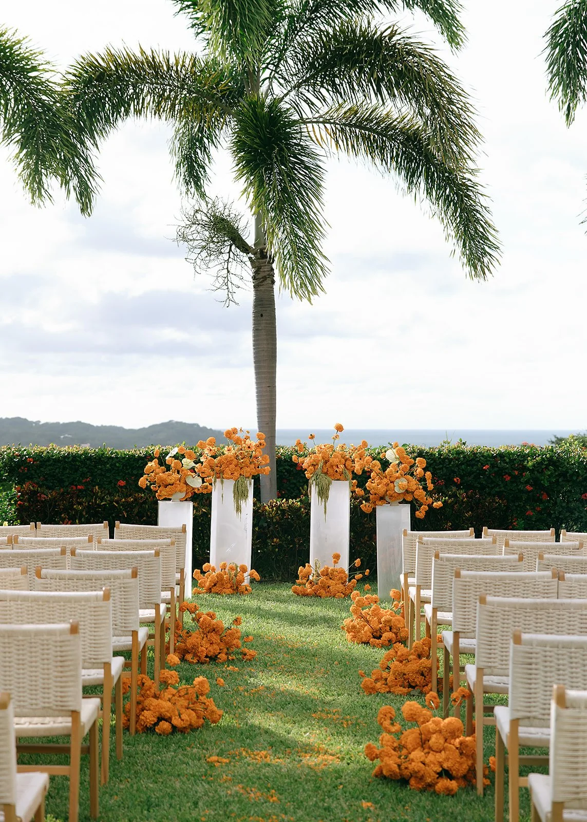 A wedding altar decorated marigolds and orange flowers, set up outdoors near palm trees with a view of the beach in the background. In Nayarit, Mexico