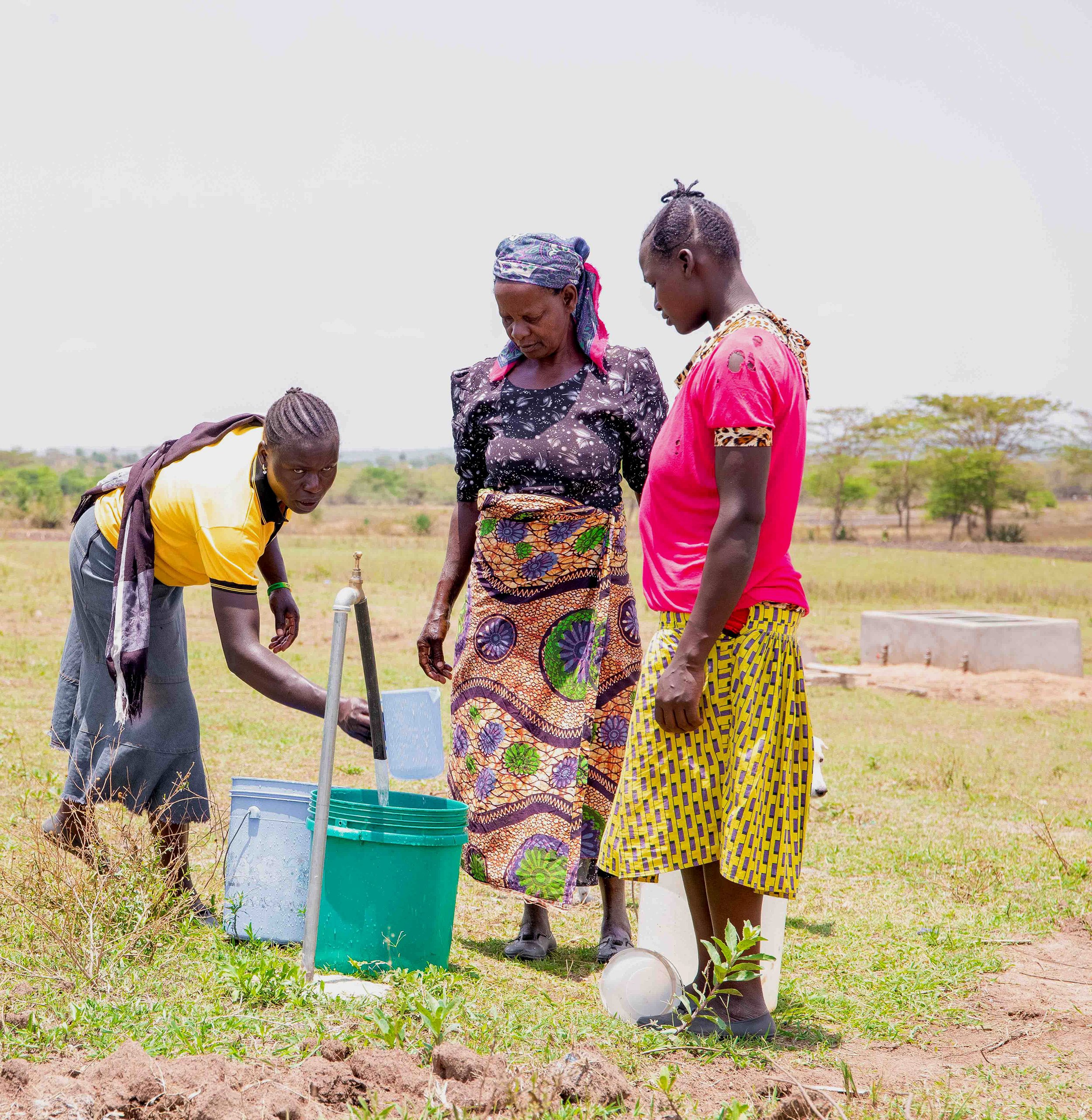 Women gathered around a water faucet outdoors, filling buckets with water.