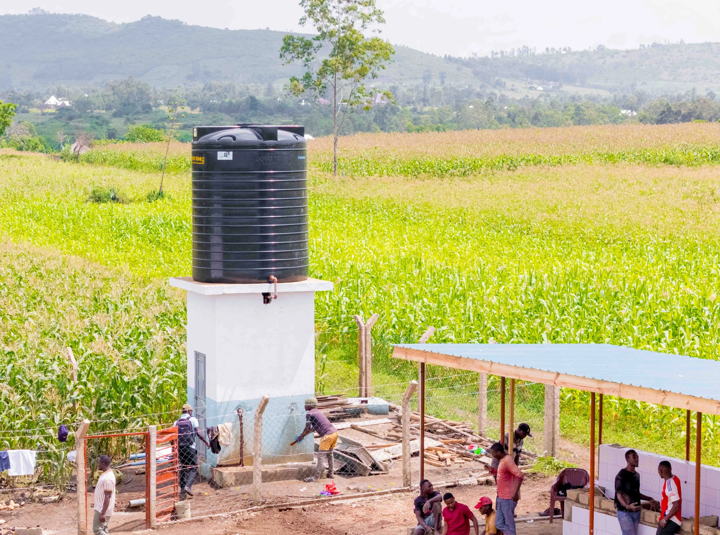 People working on WASH Hub No. 2 near farmland and mountains, with a water tank.