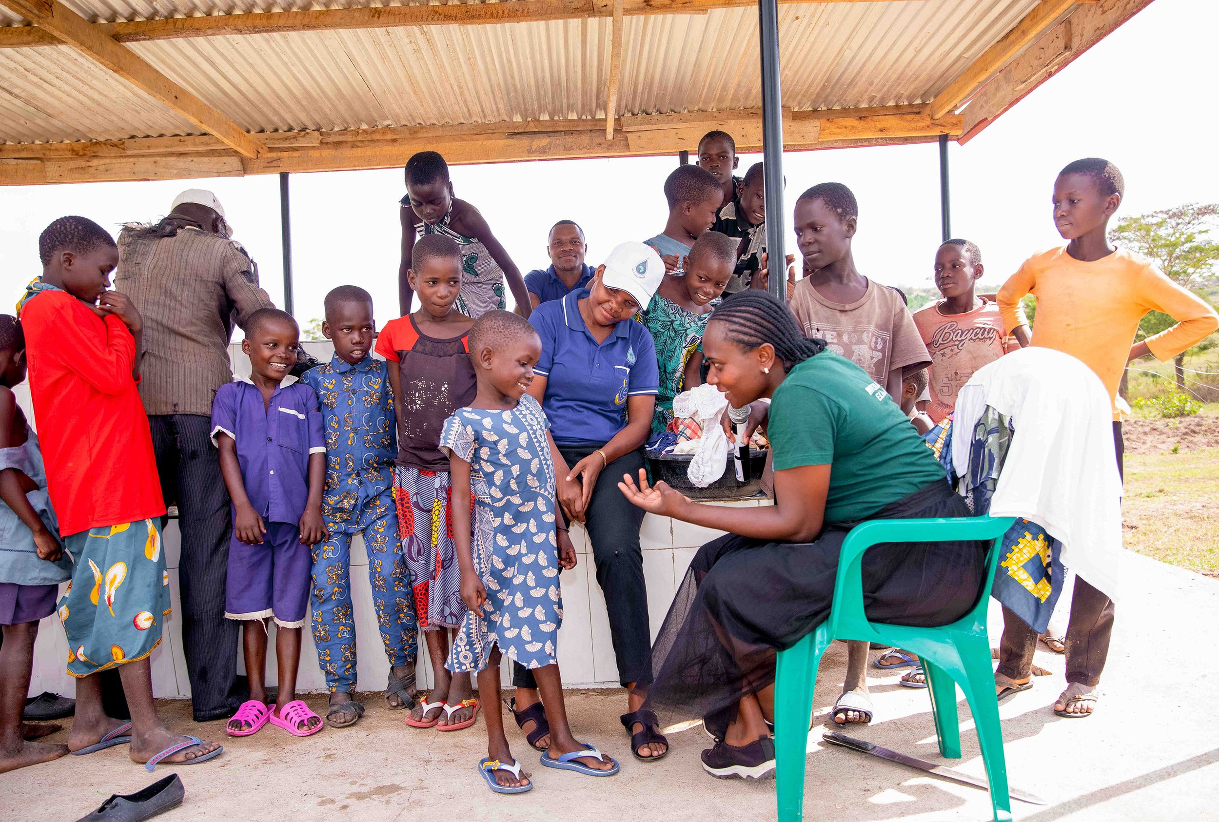 Group of children and MSG team member gathered under a wooden roof for community event.