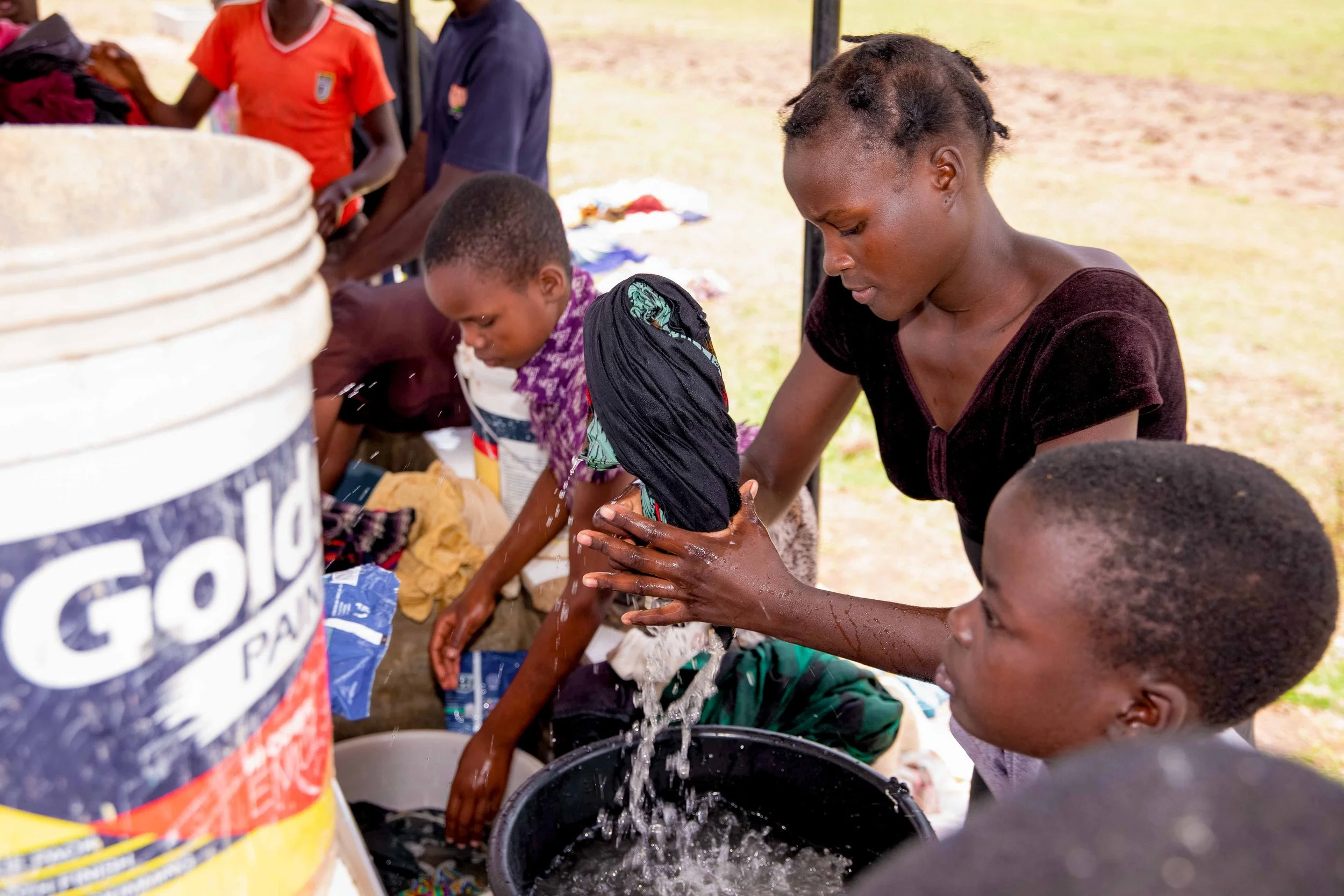 Children and adults washing laundry at WASH Hub water station..