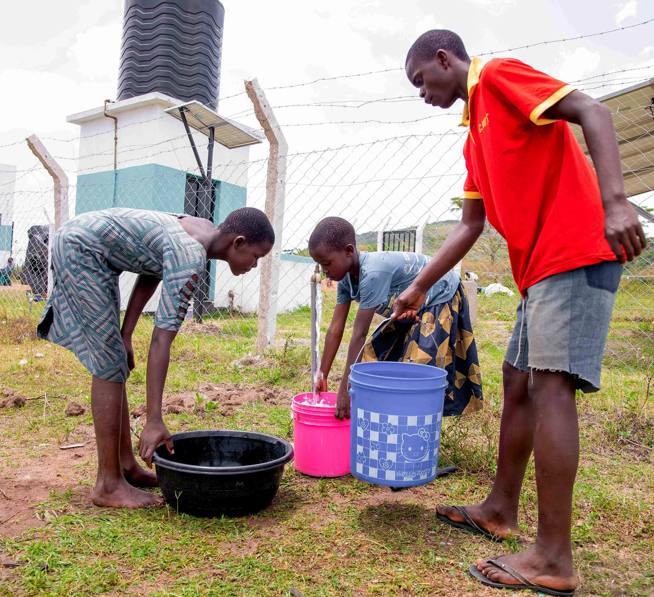 A group of boys gathering around and working with buckets of water..