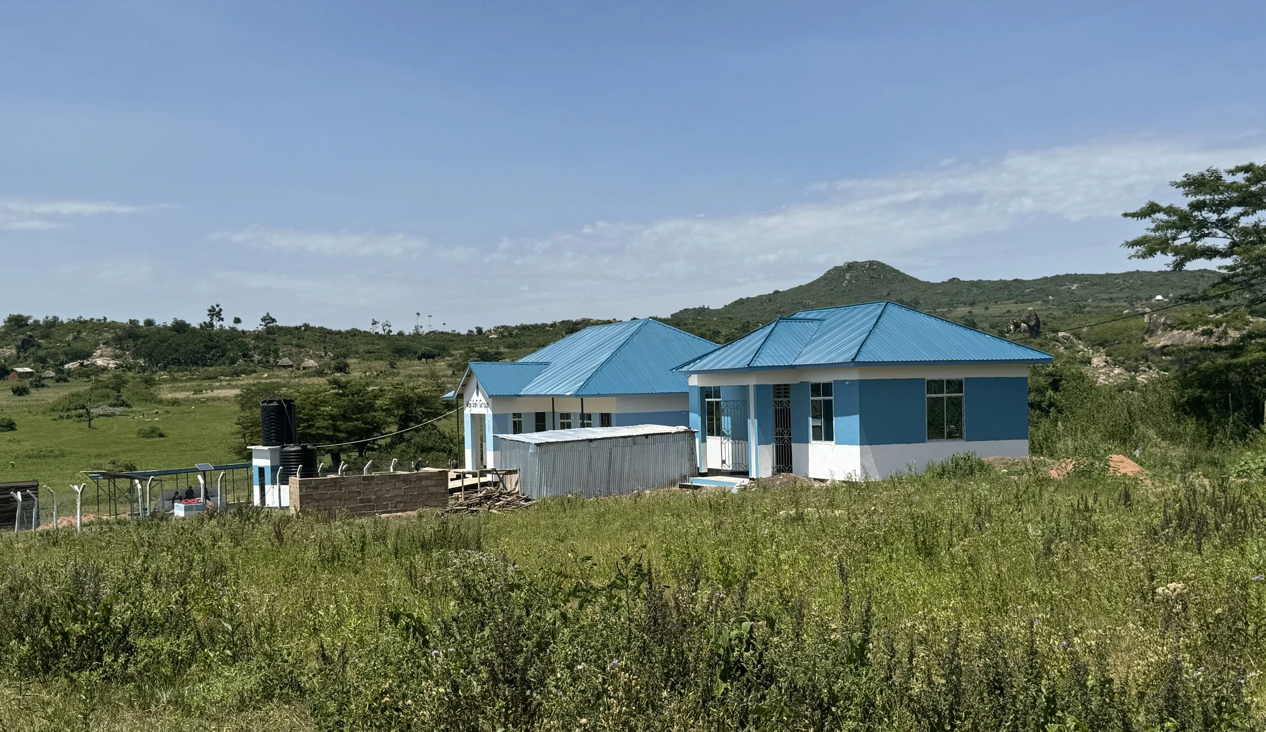 A rural landscape with WASH Hub No. 1 surrounded by grassy fields and distant hills.