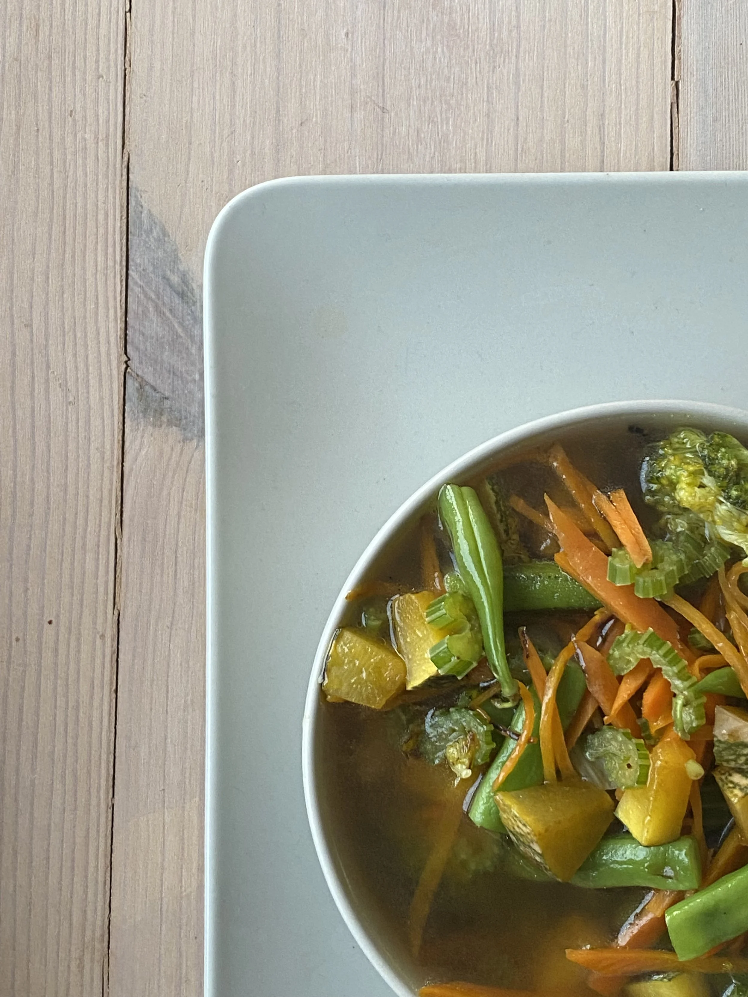 A bowl of vegetable soup on a wooden table.