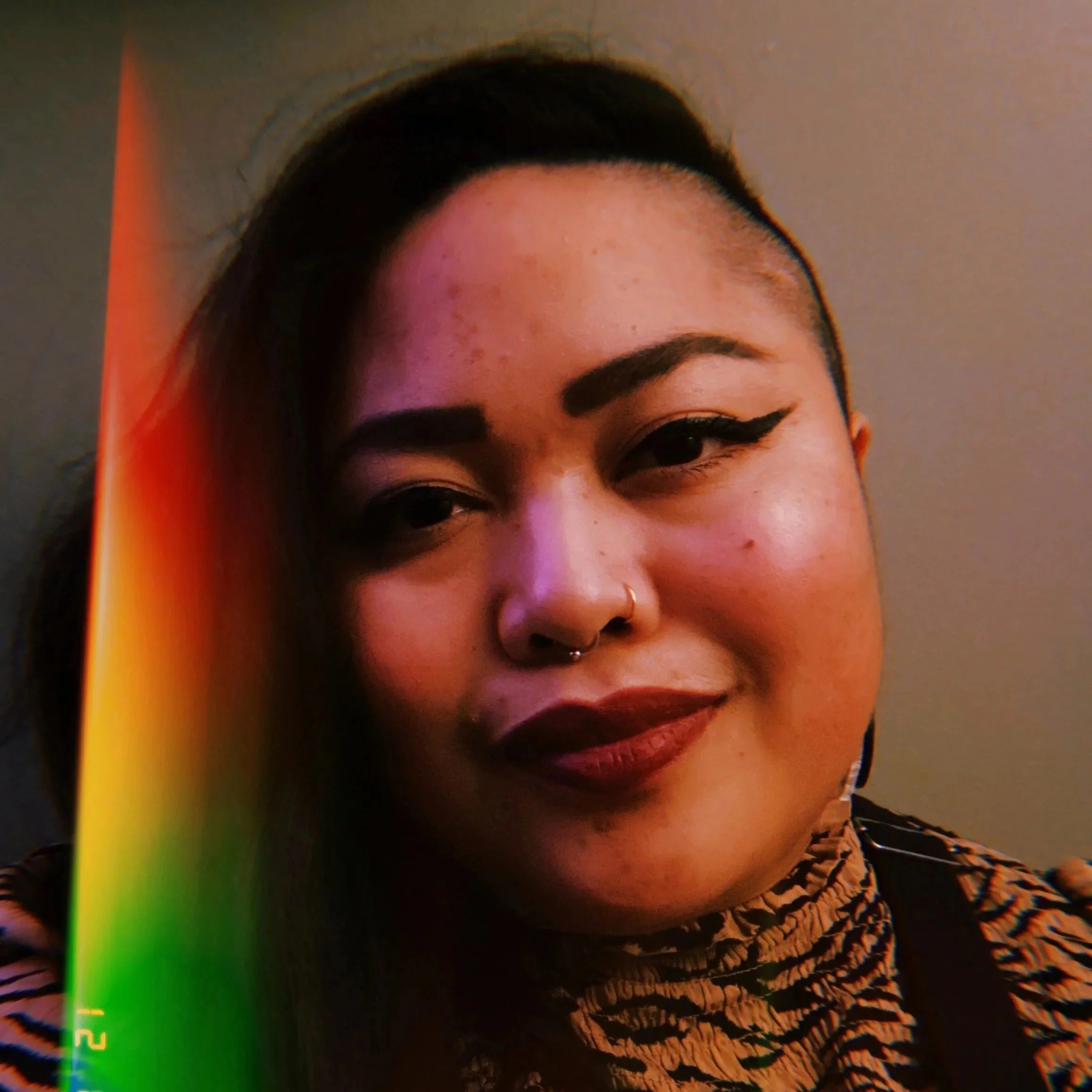 Lourdez Velasco, brown person with winged eyeliner and a nosering, looking into camera