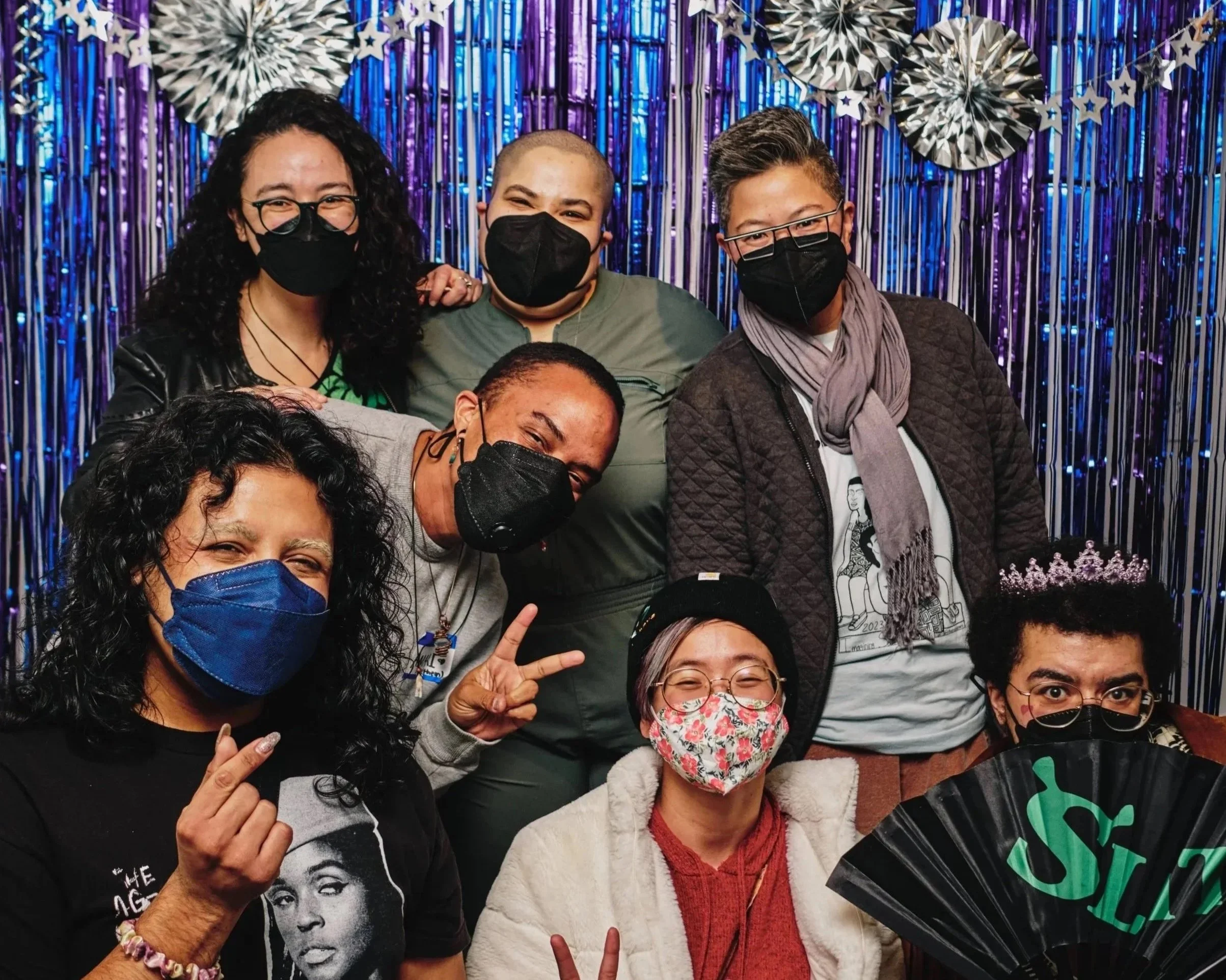 Seven members of the AAoC community posing in front of a blue and purple photo backdrop at a holiday party