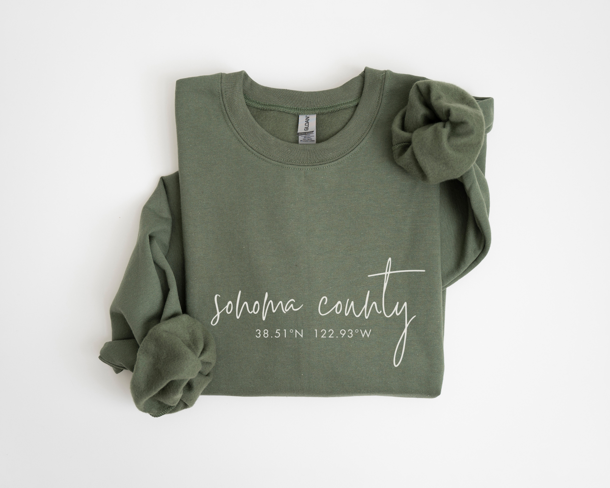 Green sweatshirt with the words "sonoma county" printed on it, with matching scrunchies attached to the shoulder, laid flat on a white background.