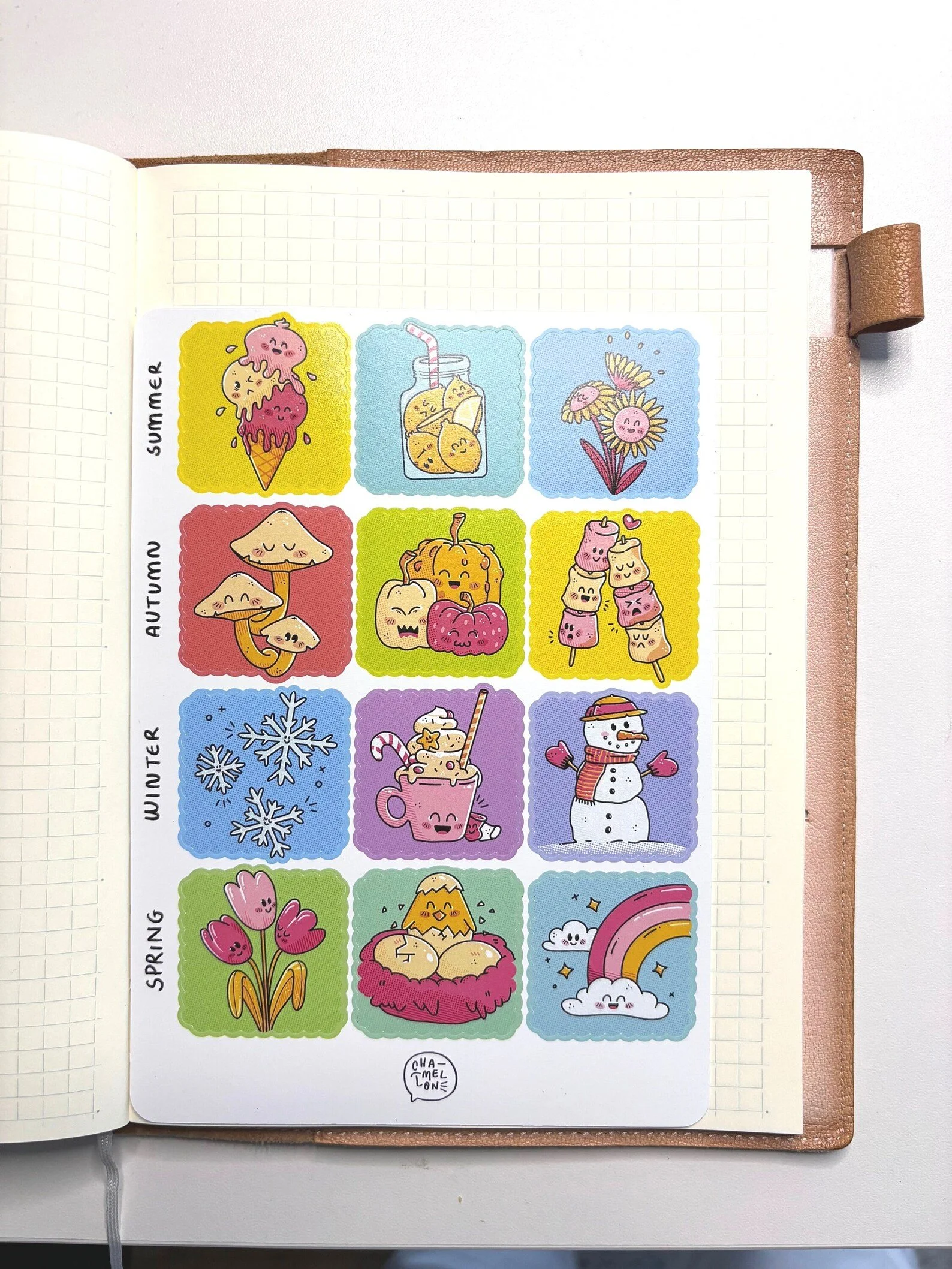 Sheet of illustrated seasonal stickers next to a bullet journal, showing the full four-season set