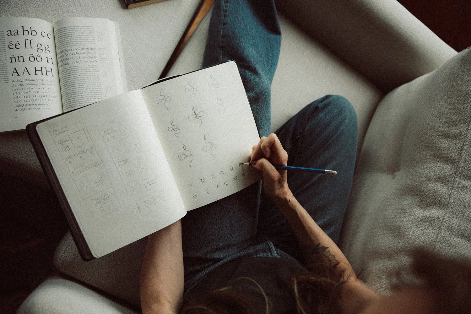 Moonstone Creative founder sketching logo concepts and zodiac symbols in a notebook alongside an open typography reference book