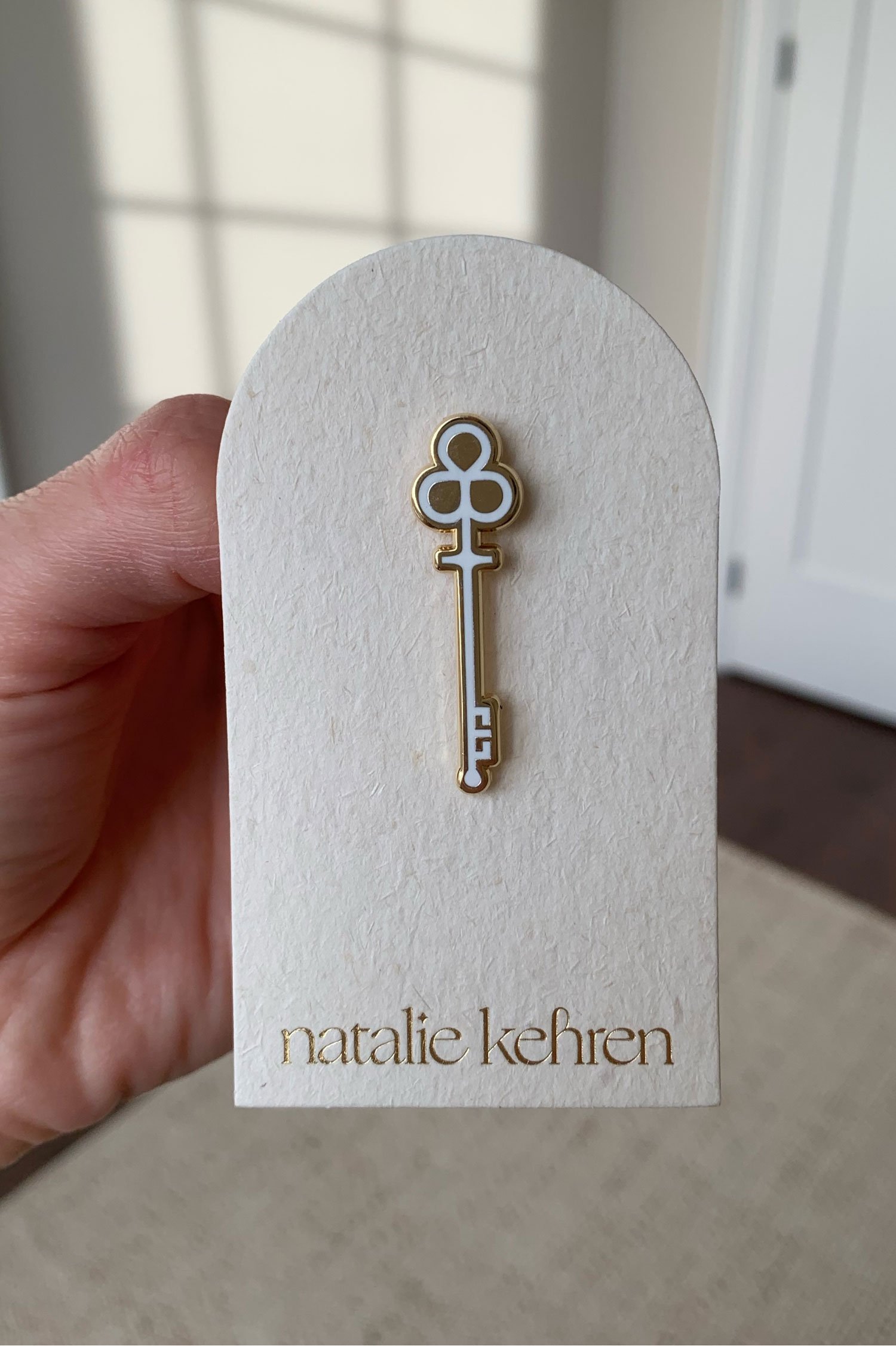 Gold enamel pin in the shape of a skeleton key afixed to an arc-shaped business card with gold foil details.